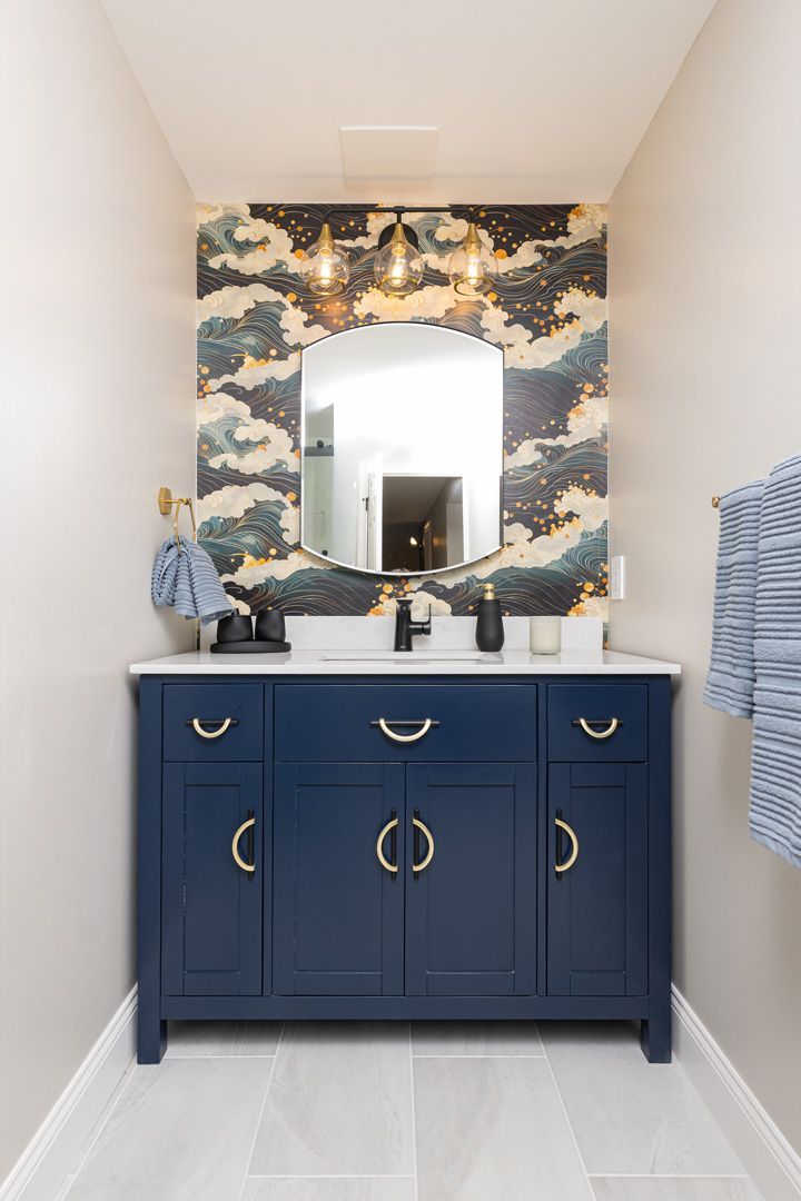 Navy vanity with gold hardware, marble countertop, and cloud wallpaper in a bathroom.
