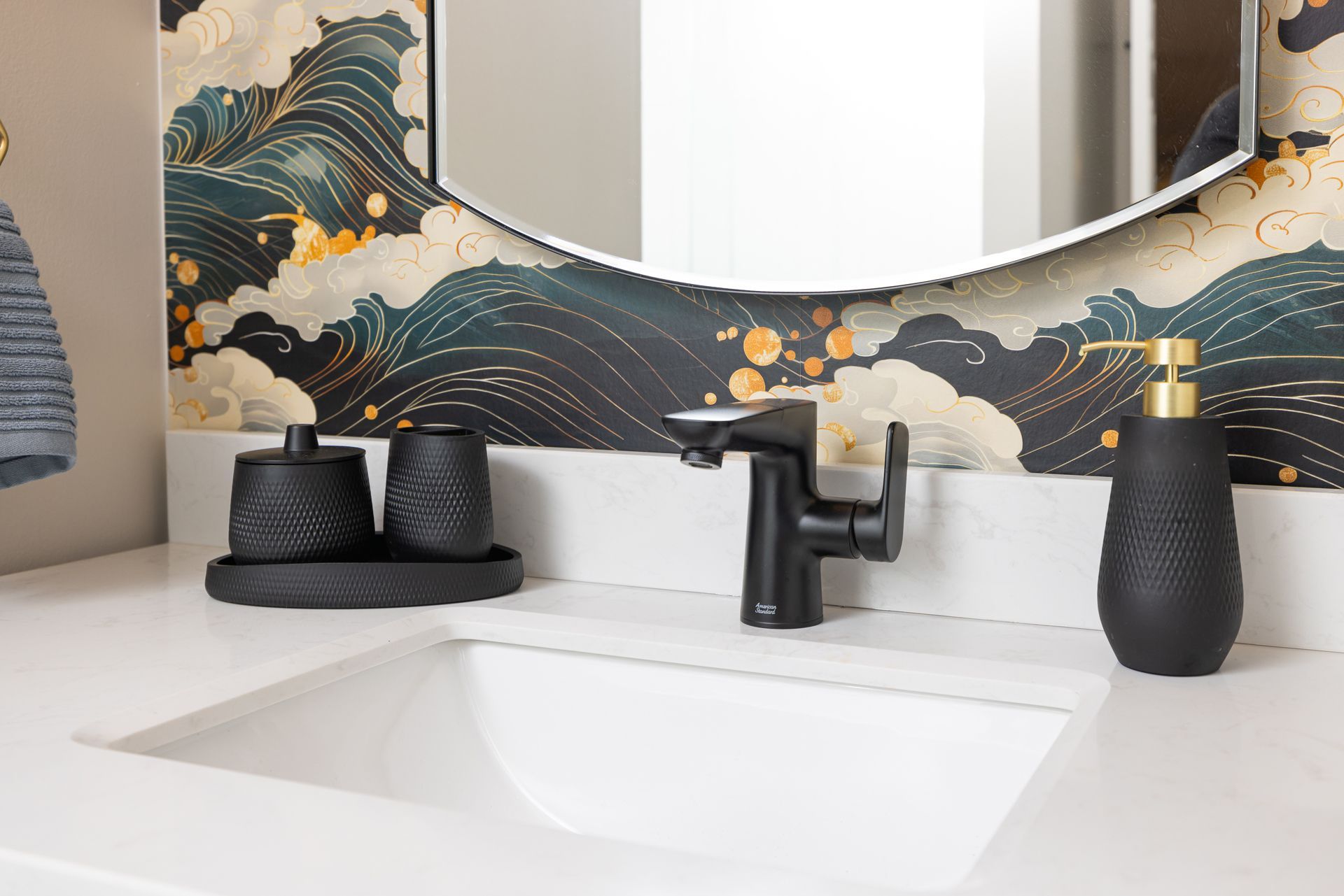 Bathroom sink with black faucet, accessories, and patterned wallpaper.