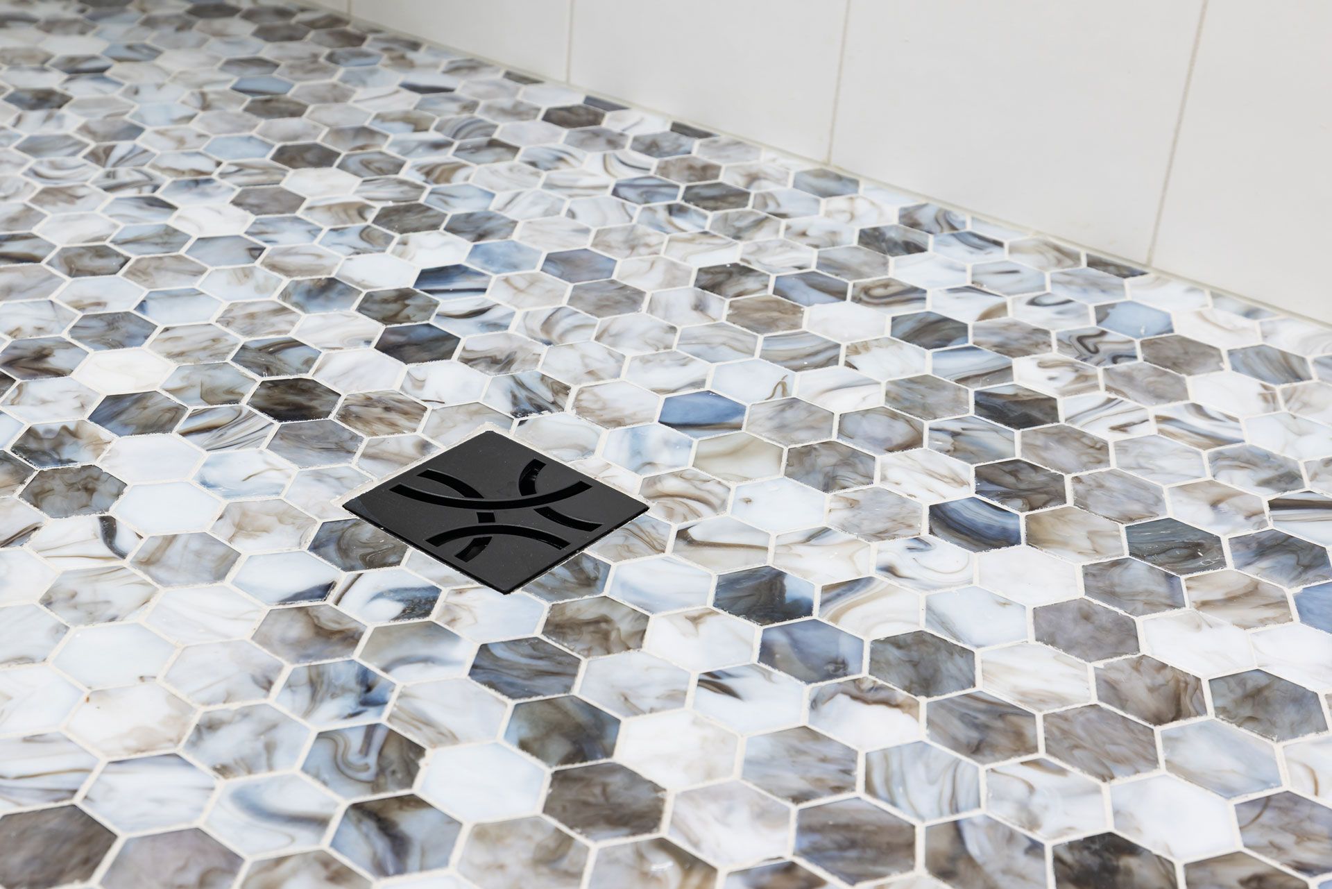 Shower floor with mosaic hexagon tiles, featuring a black drain cover with a decorative design.