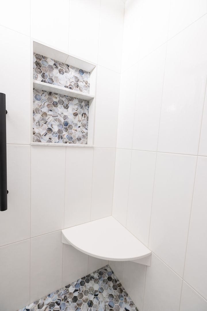 White tiled bathroom with a built-in shelf with mosaic tile accents and a corner shower seat.