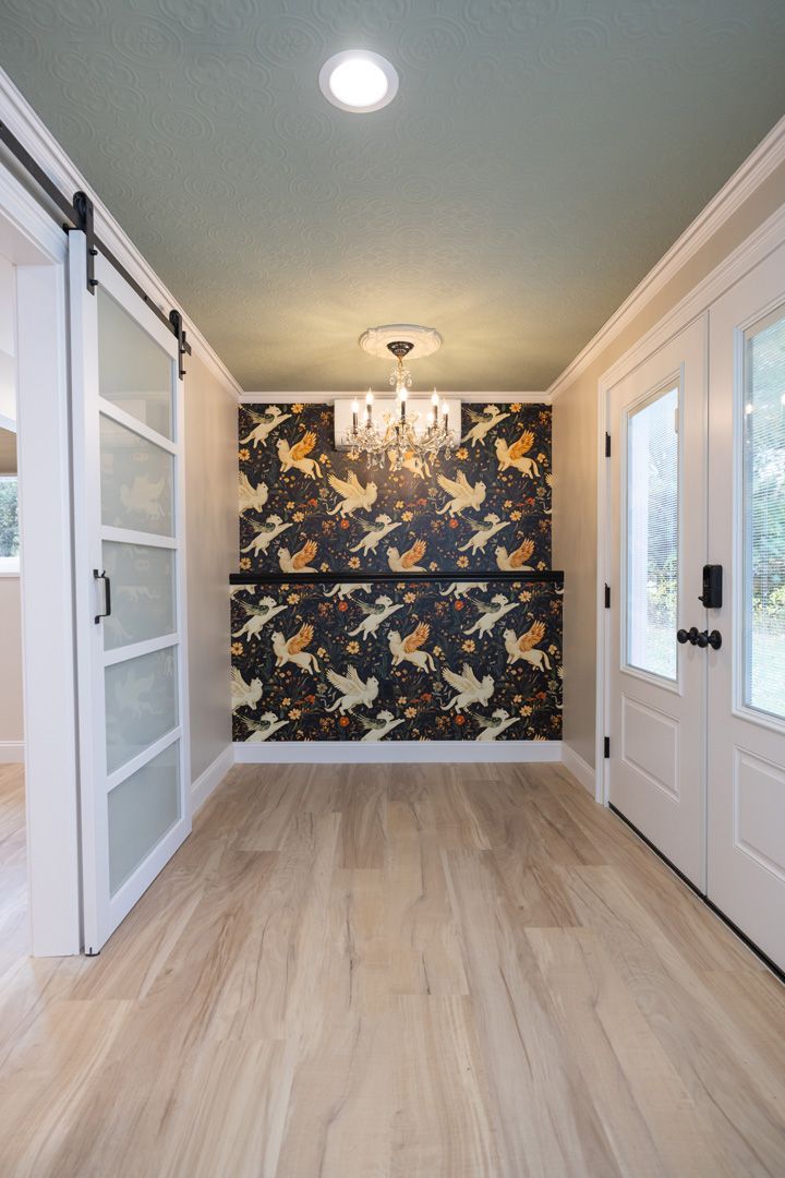 Hallway with light wood floors, a patterned accent wall, and a green ceiling.