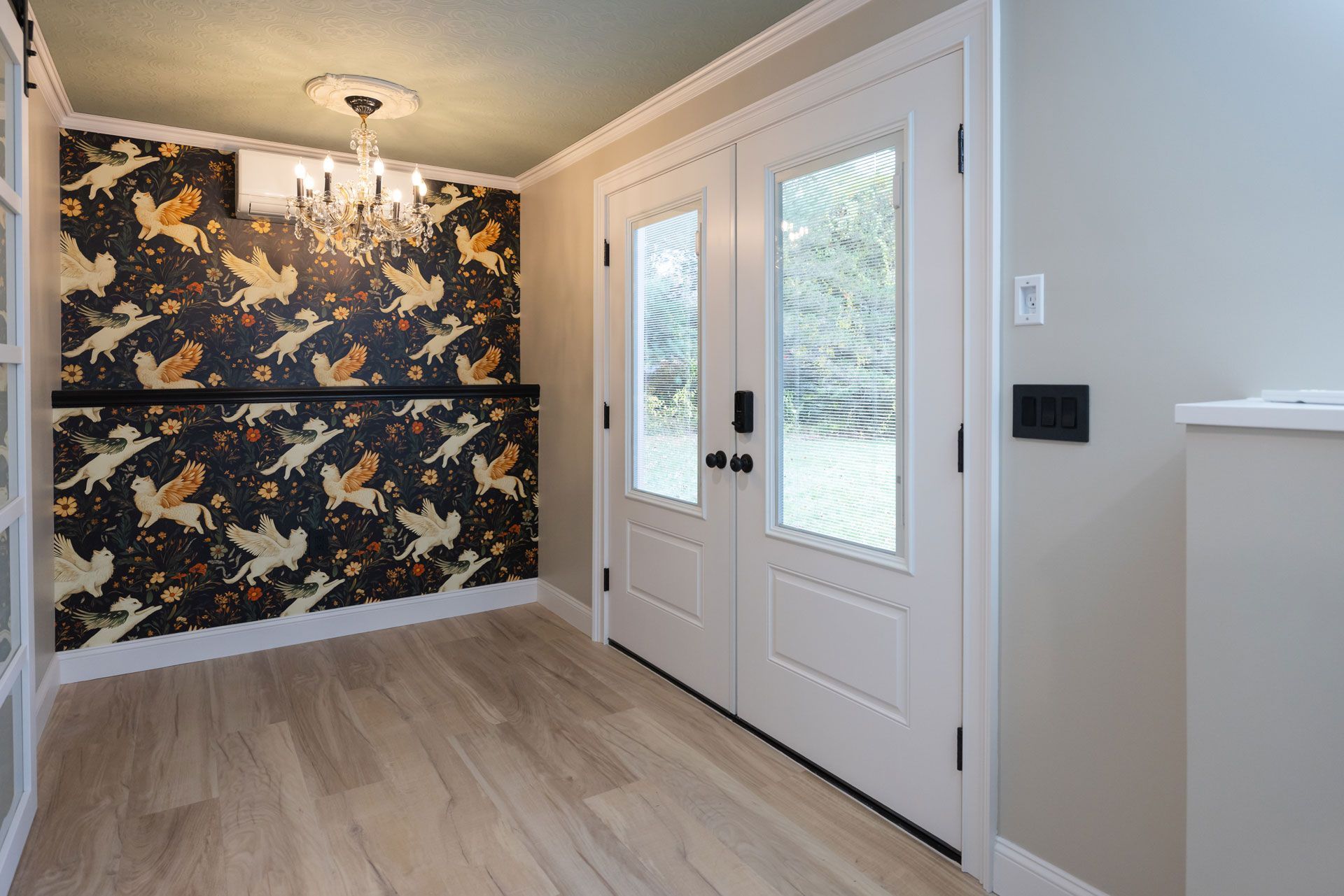 Entryway with double white doors, decorated with Halloween wallpaper, chandelier, and light wood flooring.