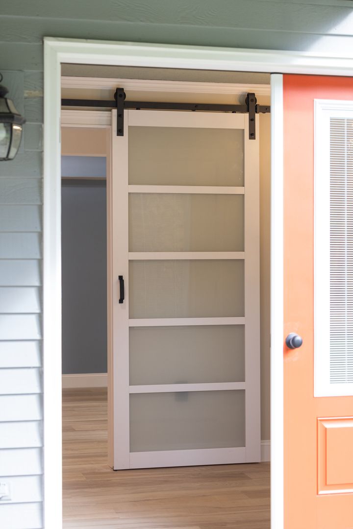 White interior sliding door with textured glass panes, black hardware, framed in white.
