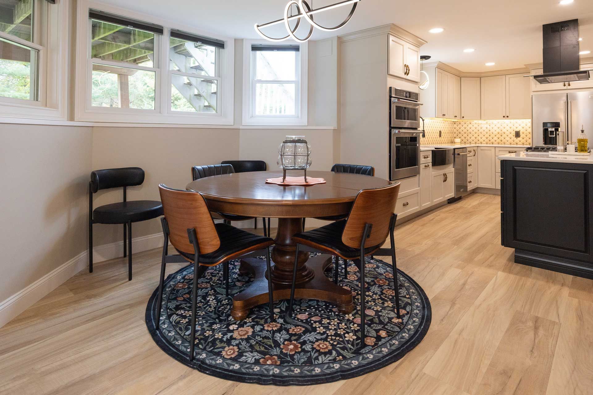 Dining area: wooden table with four chairs on a round rug, kitchen in the background.