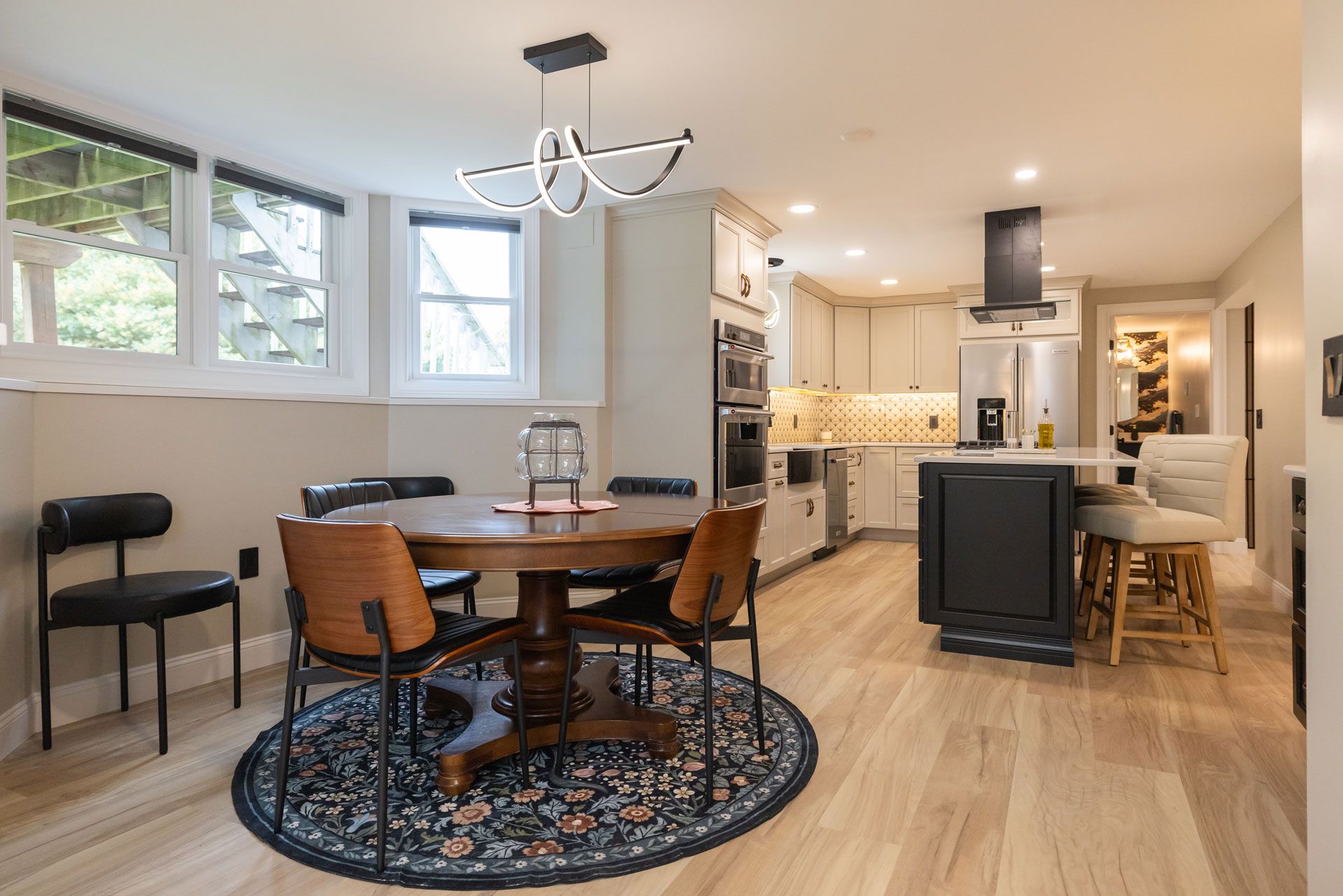 Dining area with round table, chairs, and kitchen with island. Hardwood floors and windows.