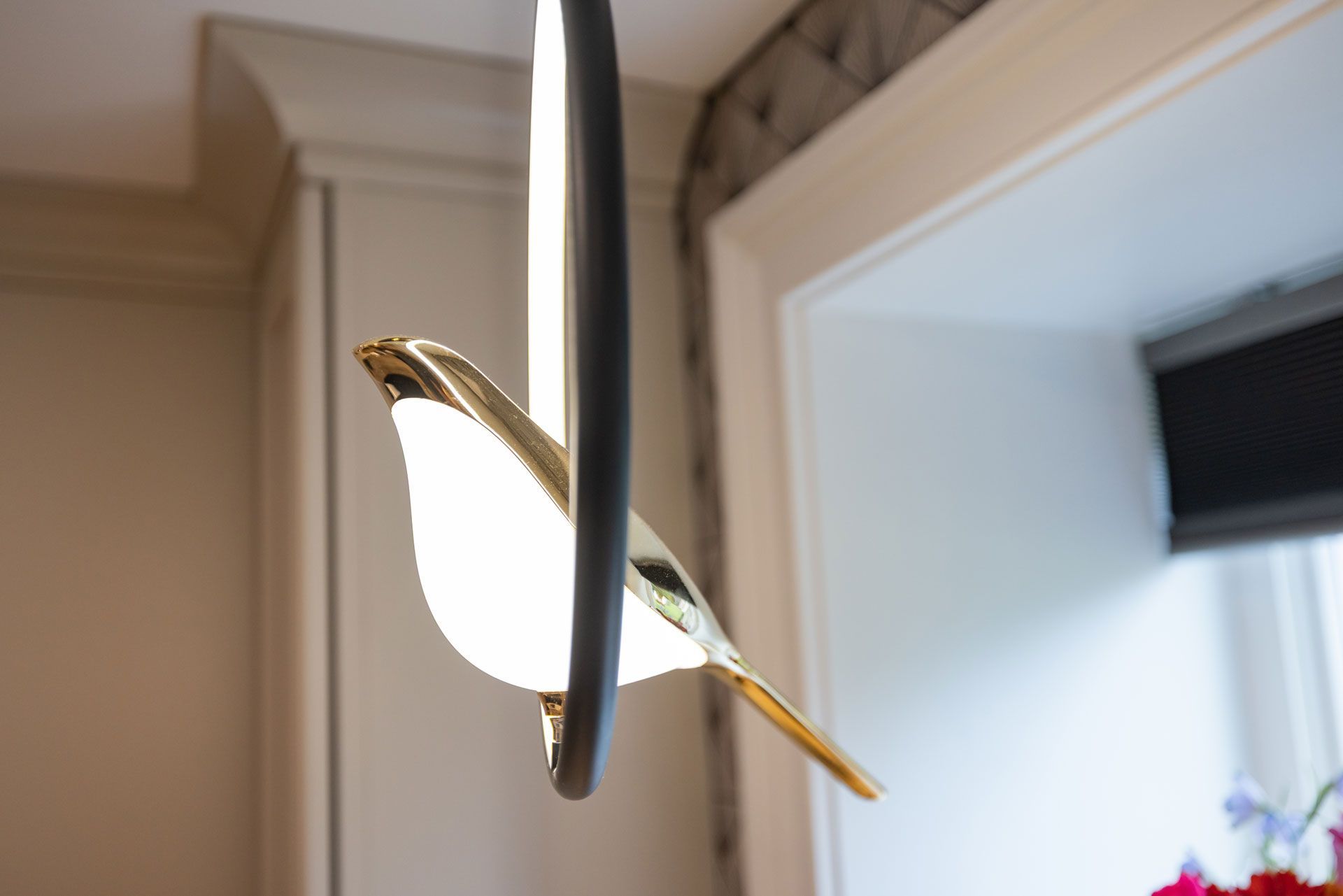Gold bird-shaped light fixture hanging in front of a window.