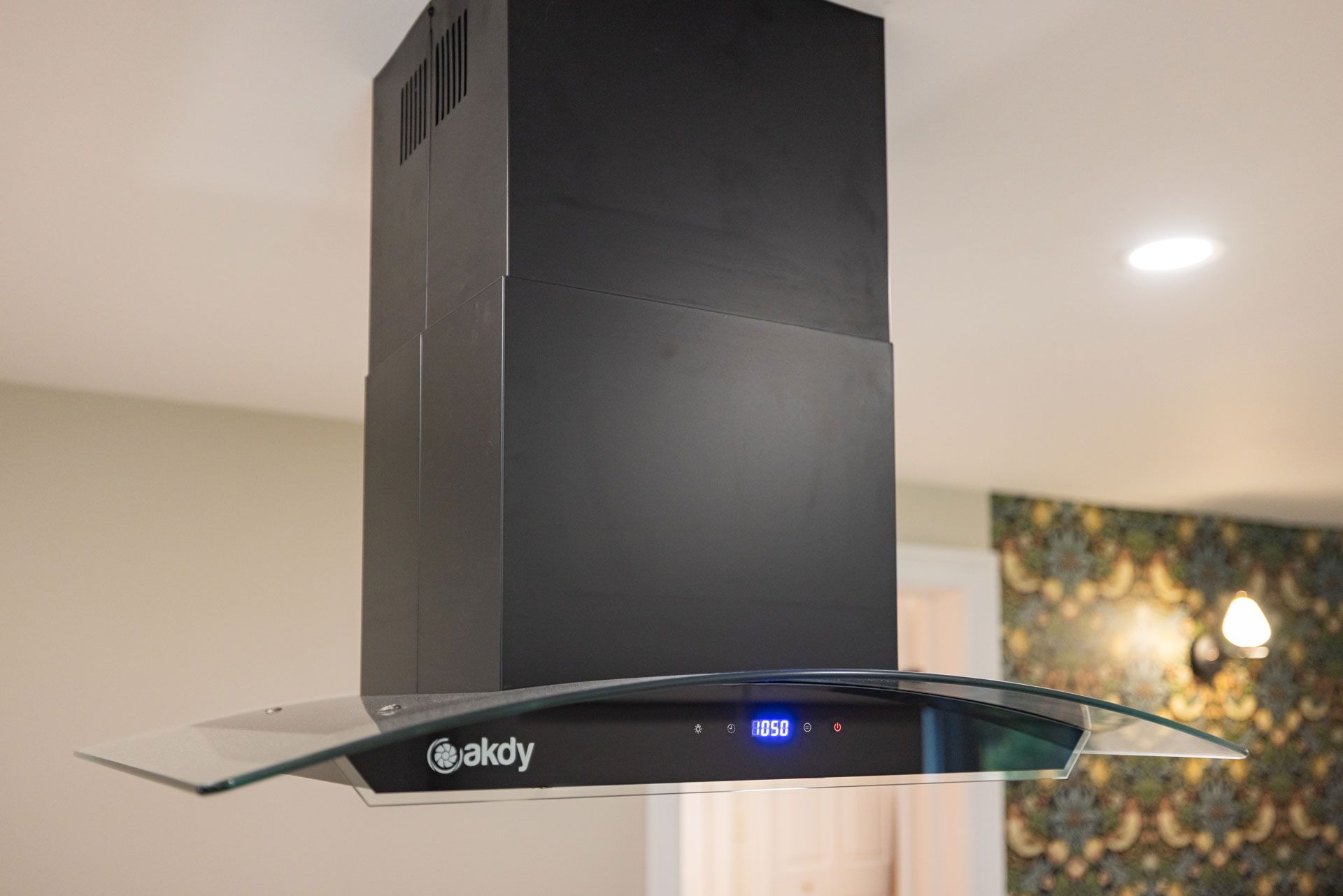 Black kitchen range hood with glass visor, mounted on a ceiling.