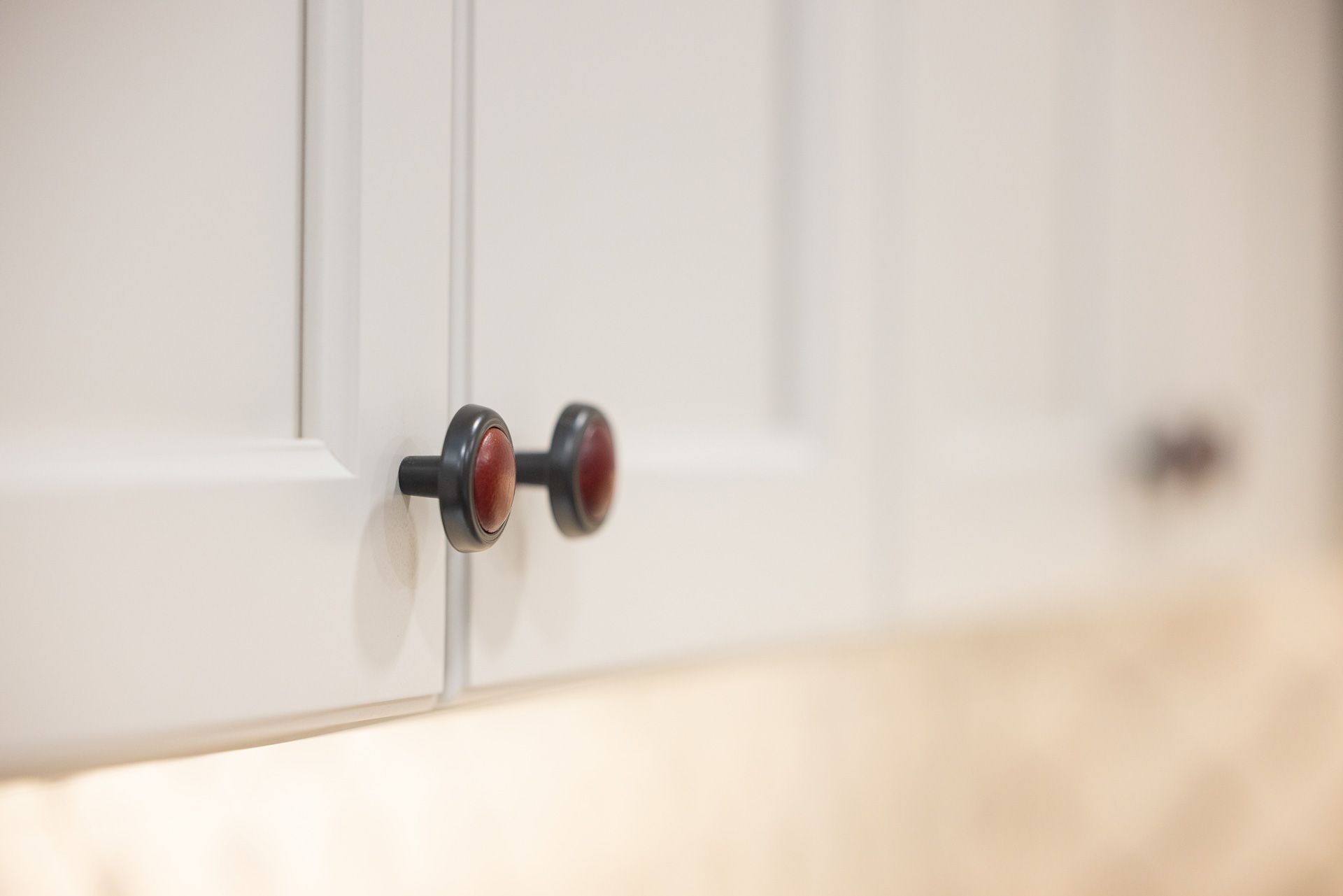 White kitchen cabinet doors with dark knobs and red accents.
