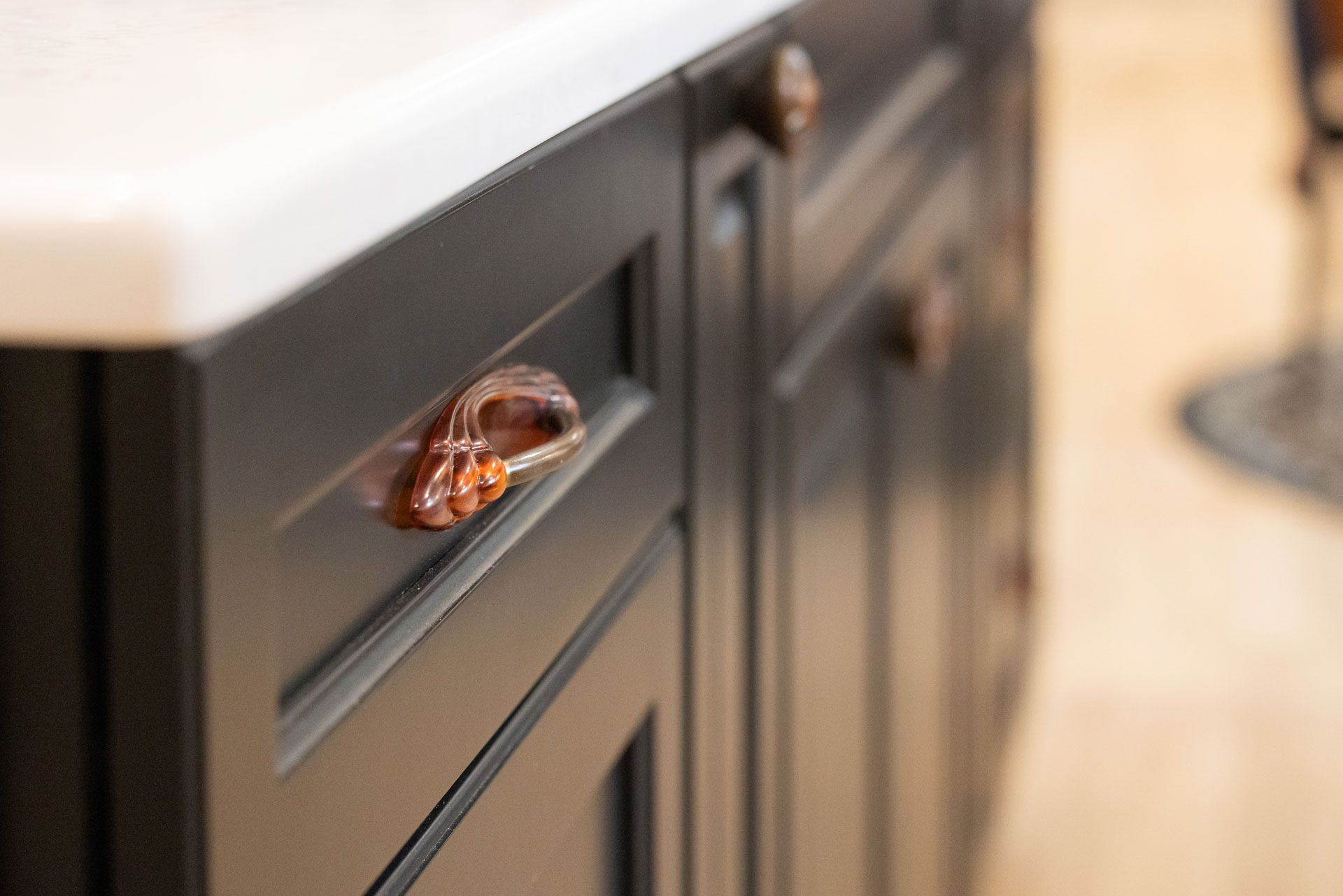 Close-up of black kitchen cabinets with copper-colored pulls, white countertop, and blurred background.