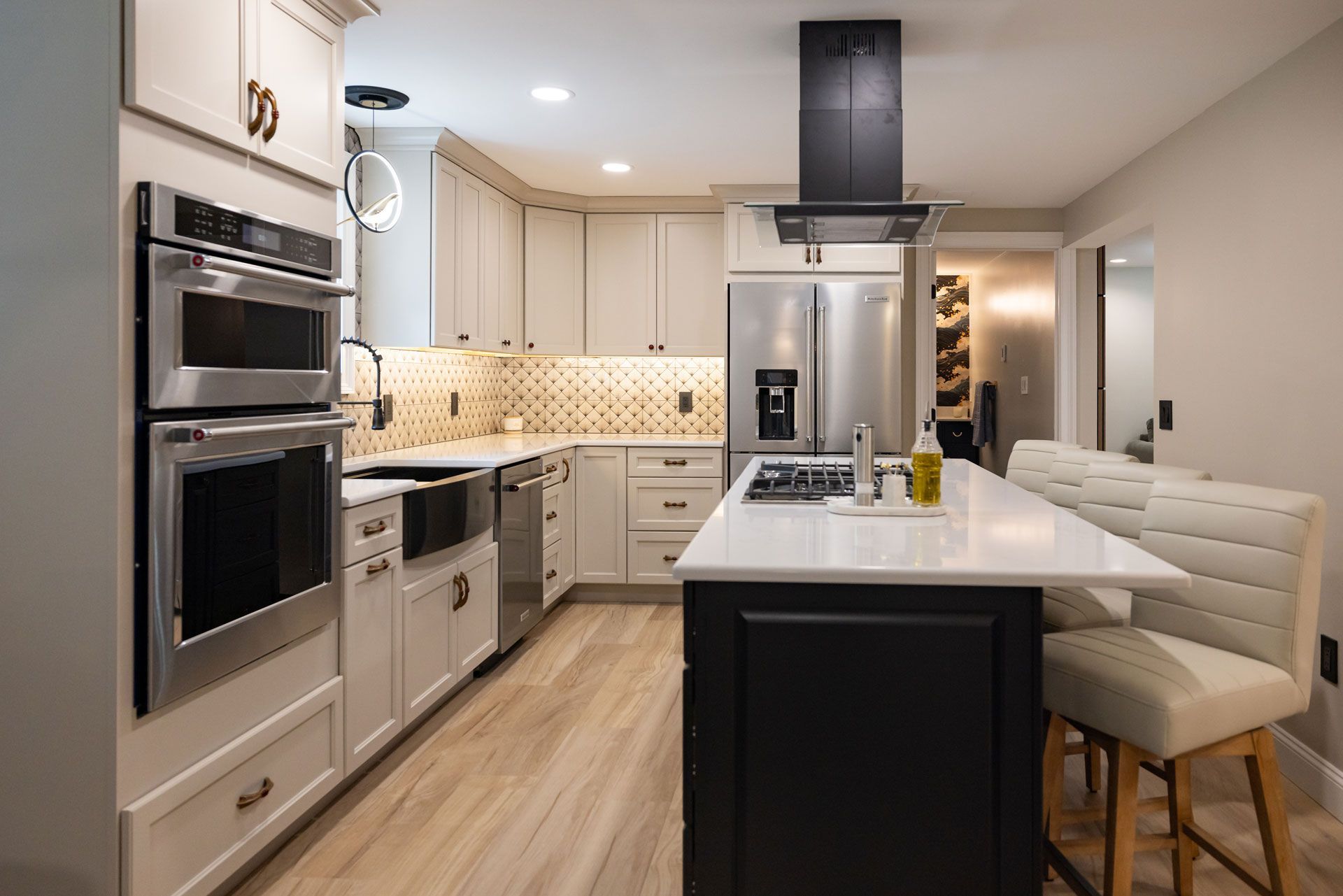 Modern kitchen with white cabinets, stainless steel appliances, black island, and light wood flooring.
