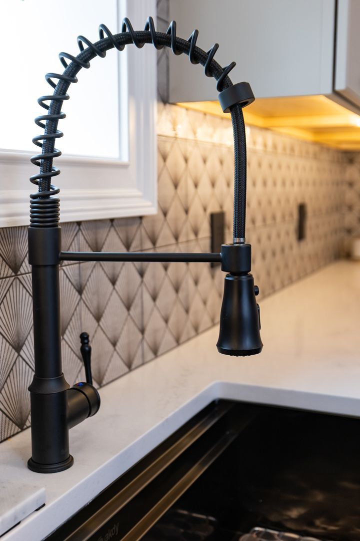 Black industrial-style kitchen faucet against a patterned tile backsplash and white countertop.