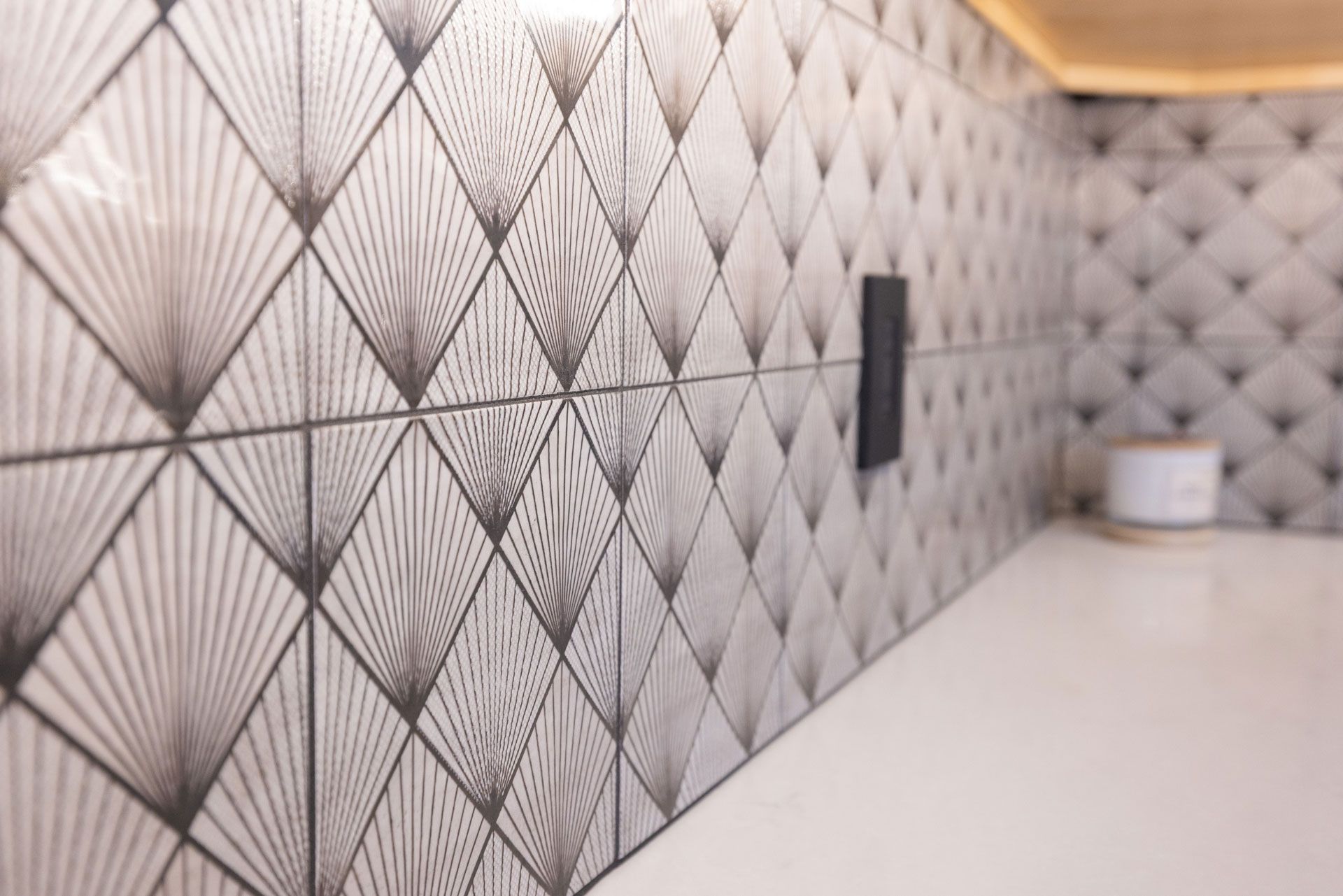 Close-up view of geometric patterned tiles in a kitchen, with a white countertop and a dark electrical panel.