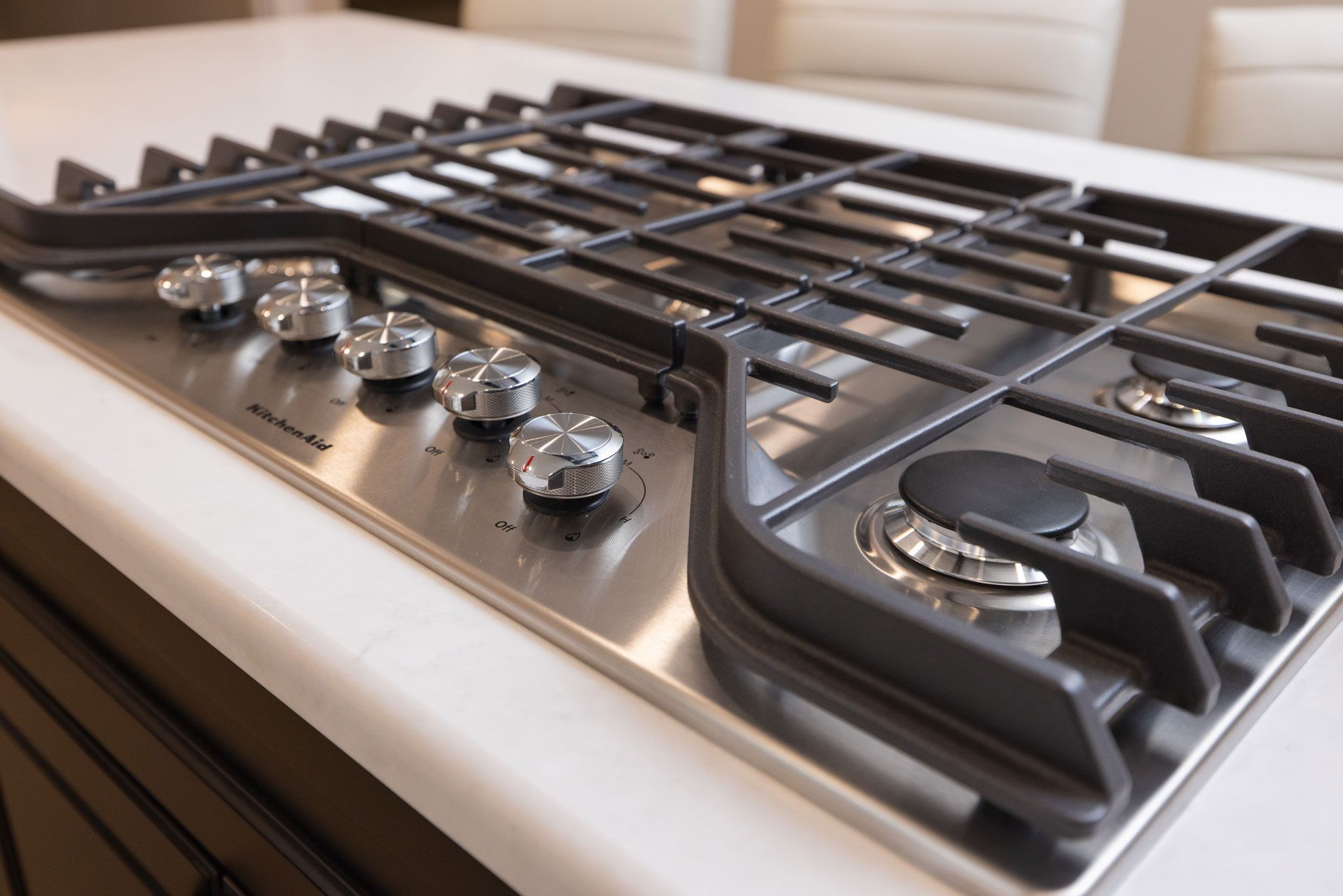 Stainless steel gas cooktop with black grates and silver knobs, built into a white countertop.