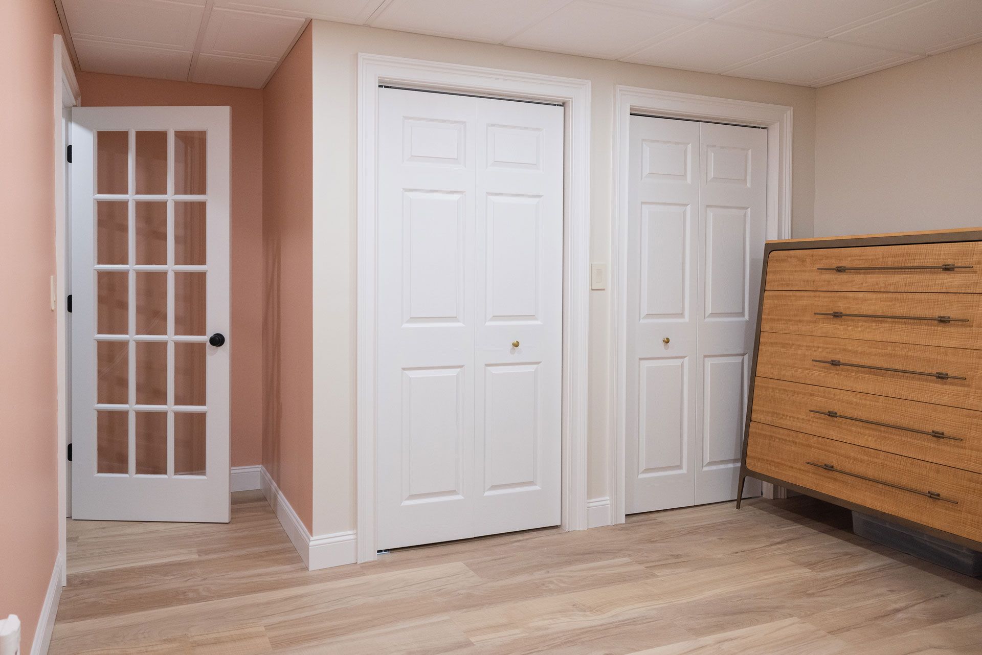 Interior room with white closet doors, wooden floor, peach walls, and glass-paneled door.