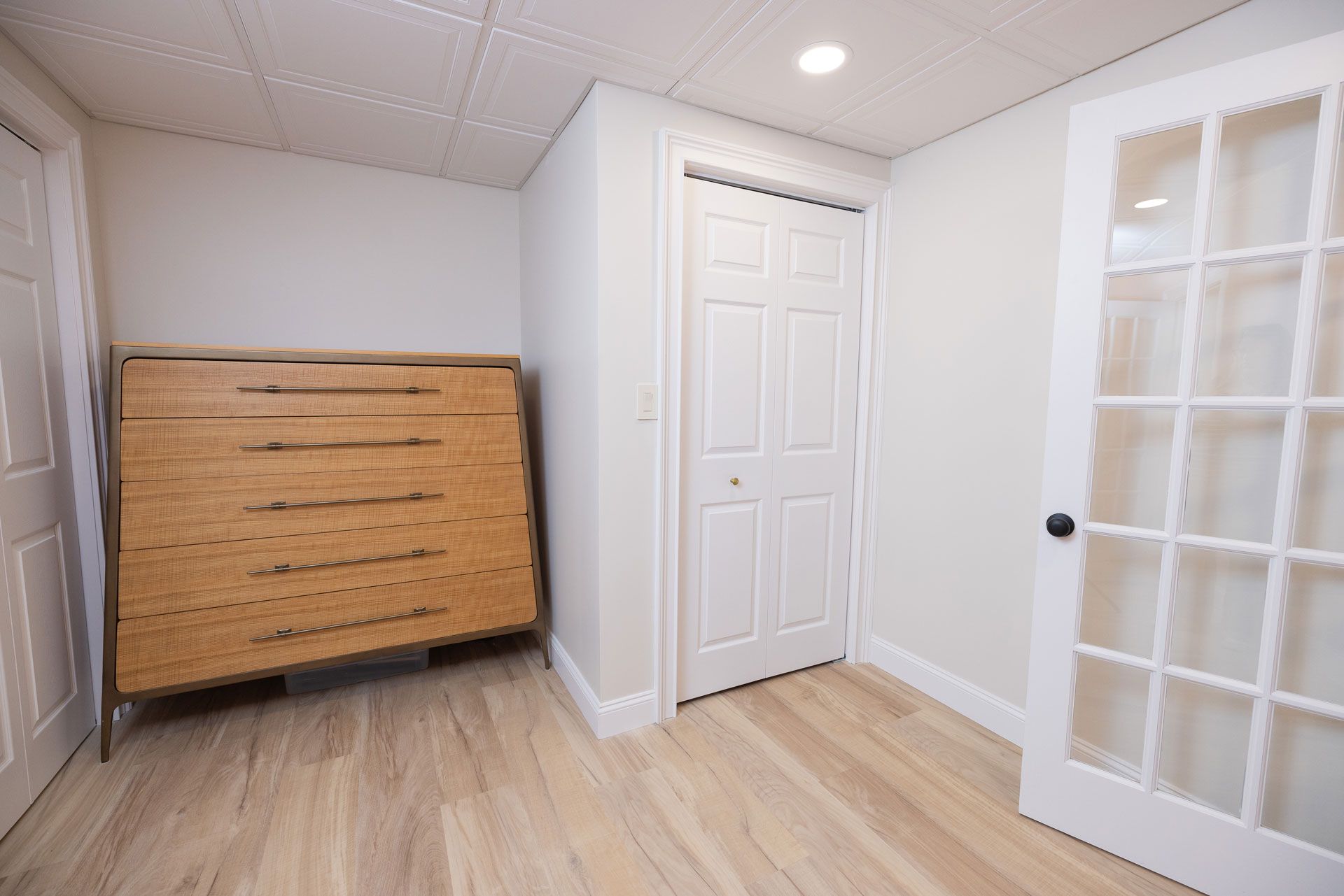 Empty room with light wood floors, white walls, closet, and a French door. A wooden chest is on the left.