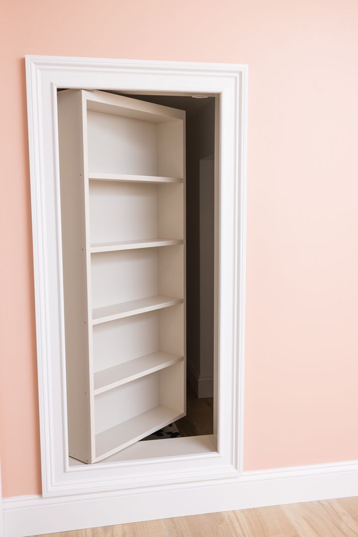 White bookshelf pivoting open, concealing a hidden doorway in a pink-walled room.