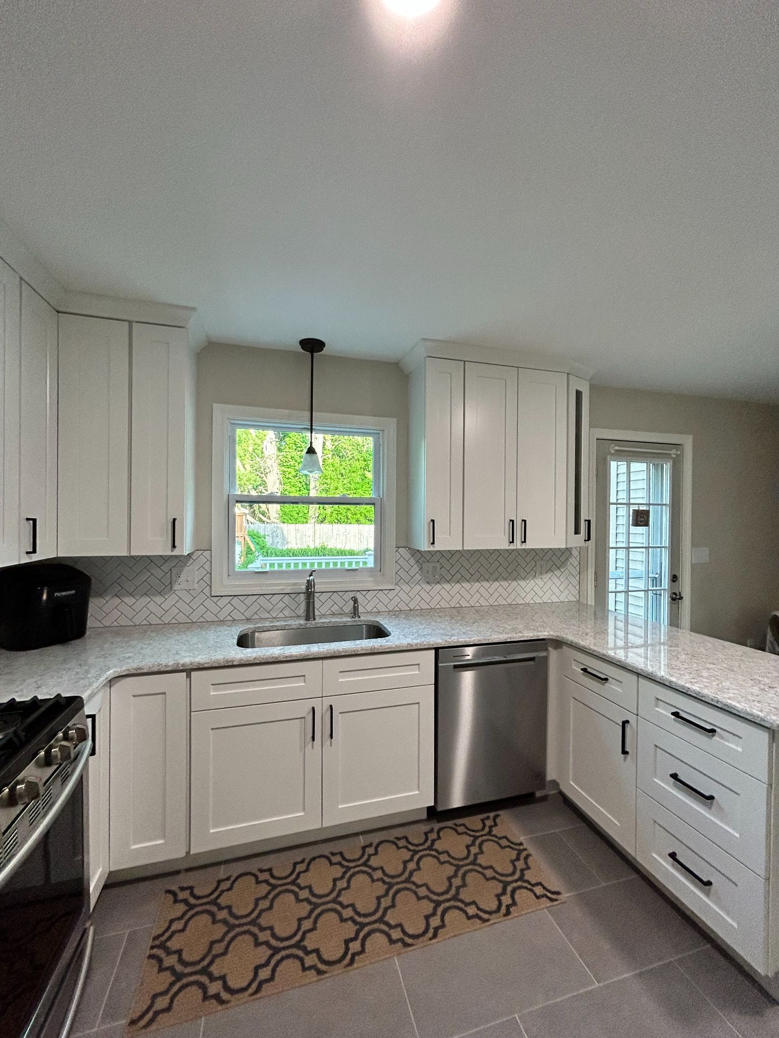 White kitchen with stainless steel appliances, white cabinets, and patterned backsplash.