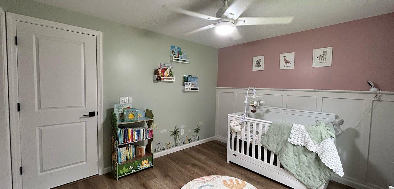 A nursery with a white crib, a small bookshelf, and artwork on green and pink walls.