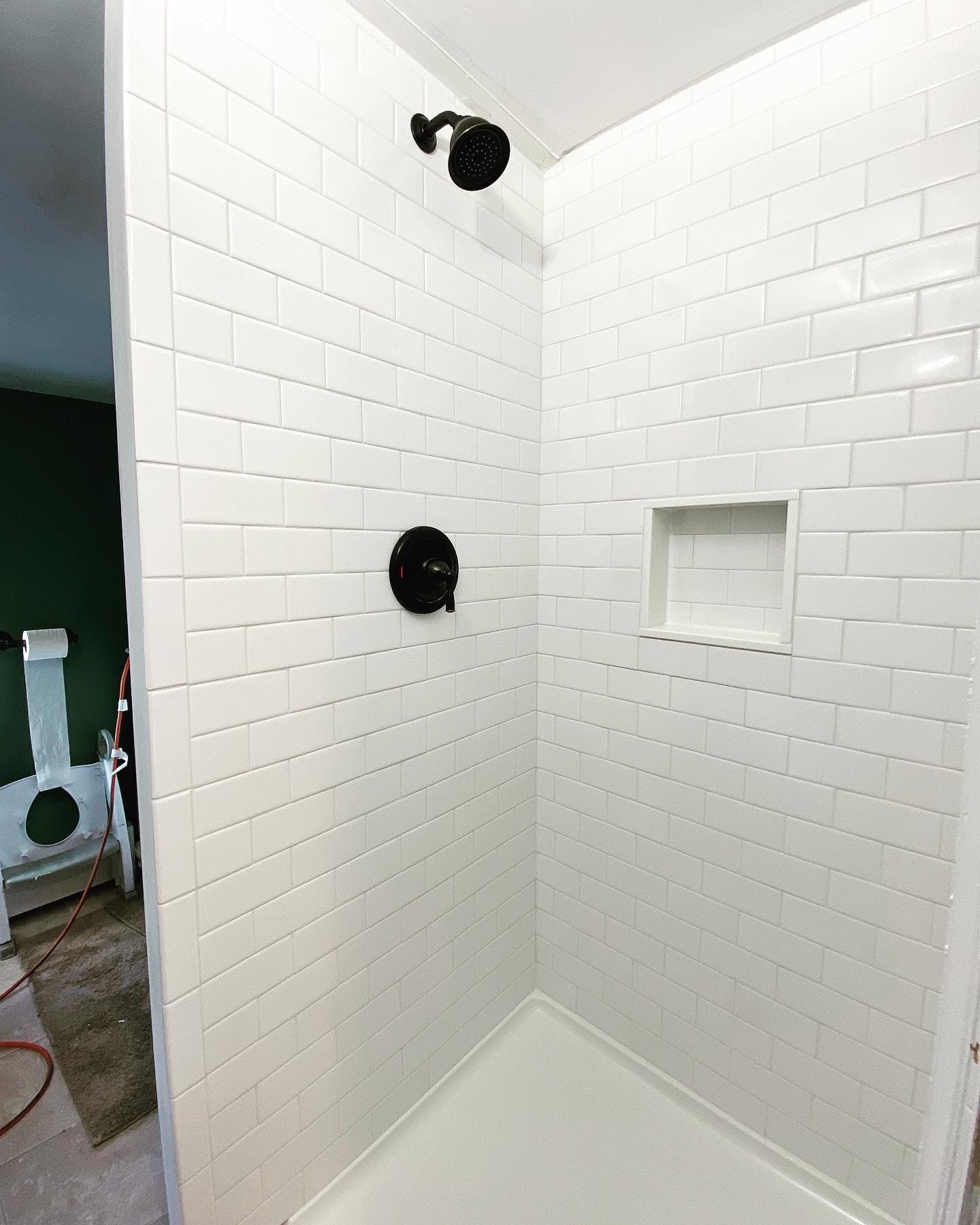 White tiled shower with black fixtures and recessed shelf.