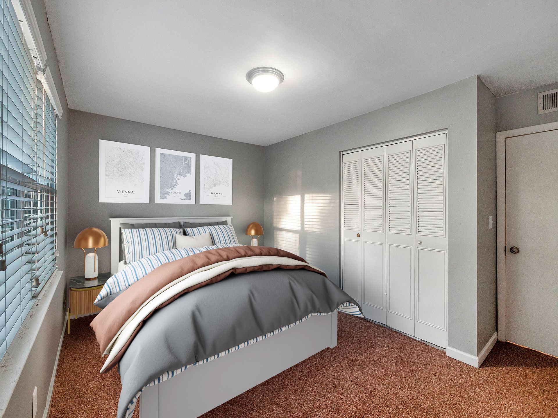 A bedroom with a bed featuring a gray and white duvet, three framed wall prints, a window with blinds, and a closet.