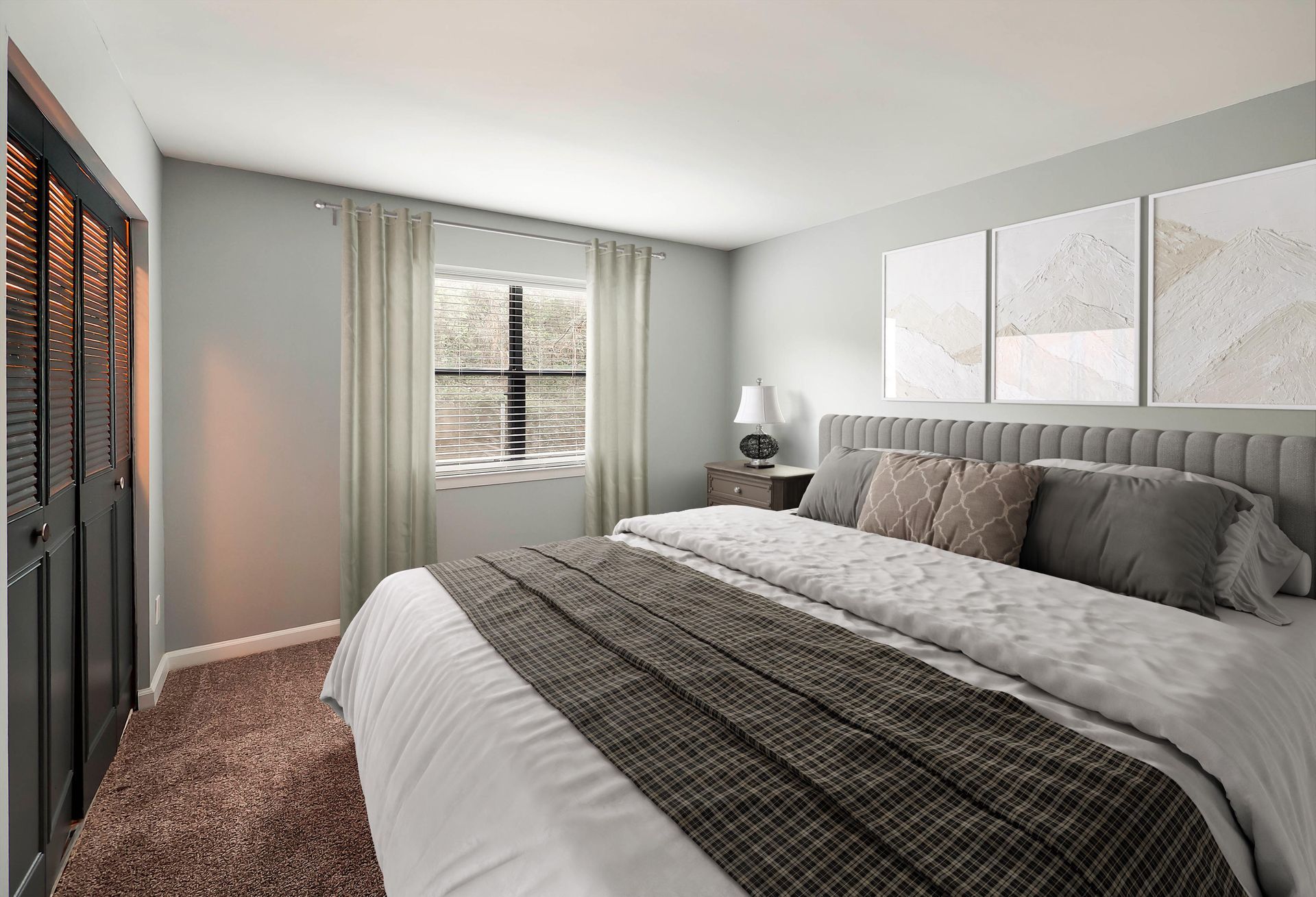 A cozy bedroom featuring a large bed with gray bedding, a dark brown carpet, and three white framed art pieces on the wall.