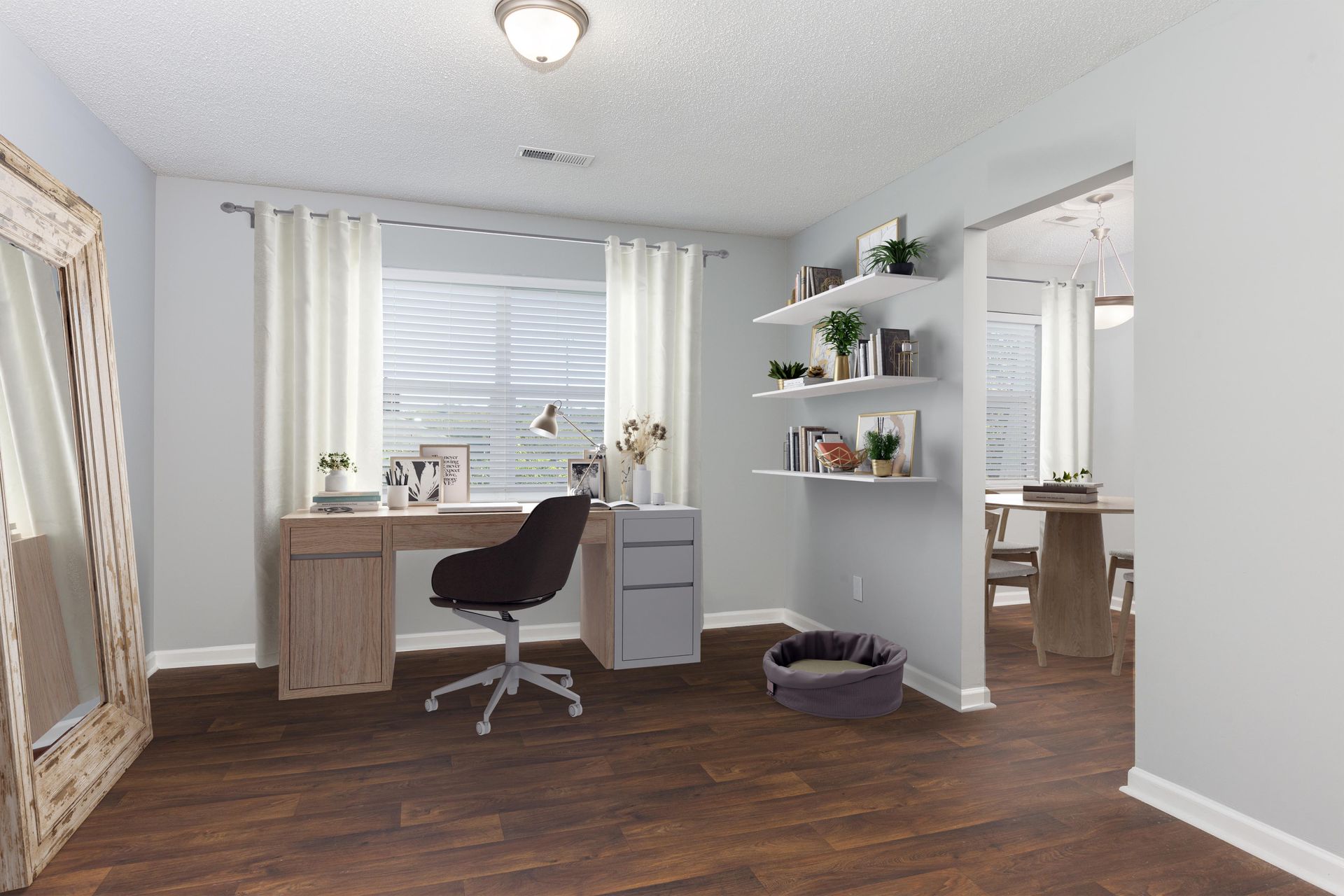 A home office with a wooden desk, an ergonomic chair, wall shelves, a large standing mirror, and a pet bed on wood floors.