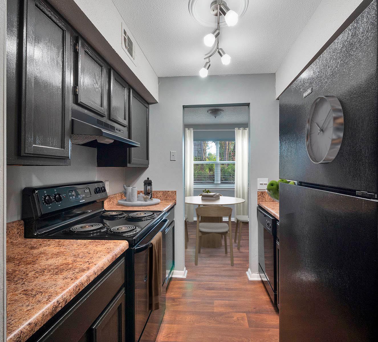 A galley kitchen with black cabinets, speckled countertops, a black stove, and a refrigerator, opening to a dining area.