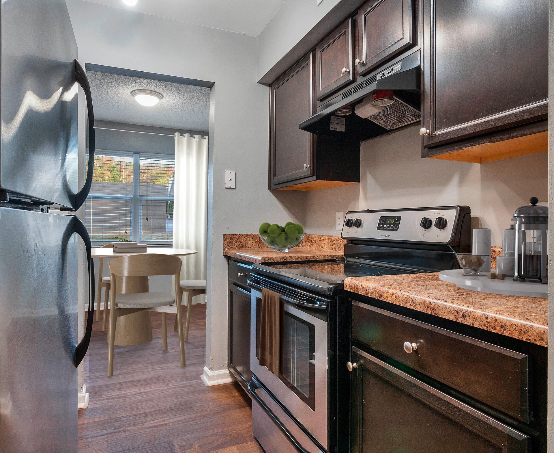 A kitchen with stainless steel appliances, dark wood cabinets, and granite countertops, leading to a dining area.
