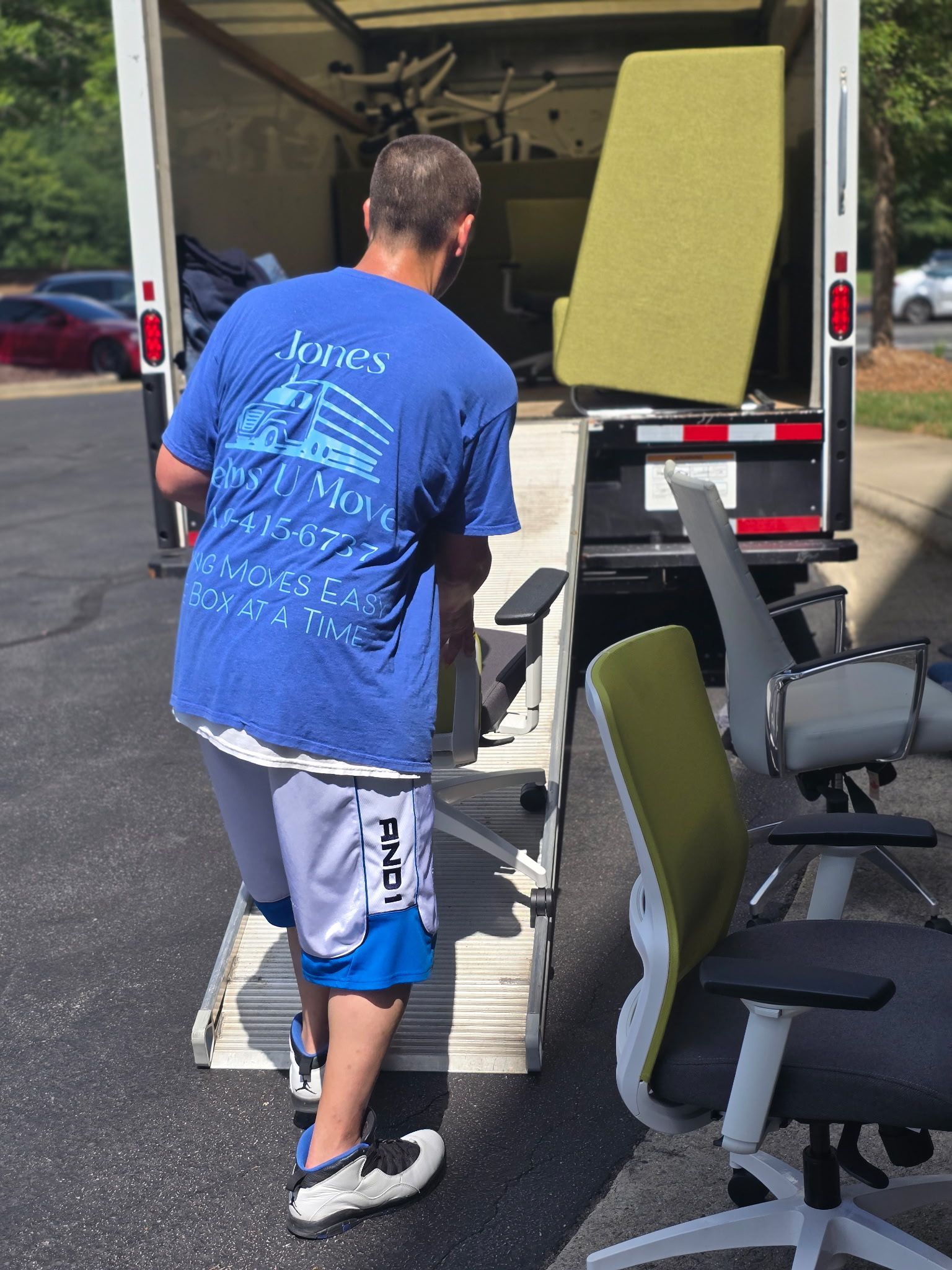JHUM team member loading office furniture onto moving vehicle and large green office lounge seating. 