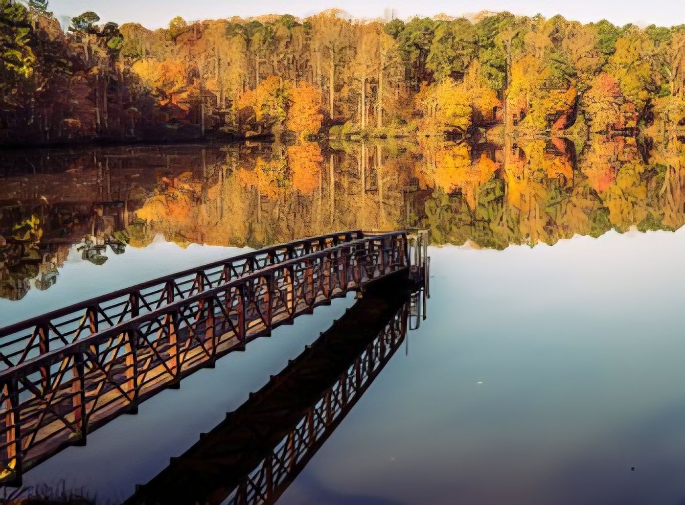 Wooden dock extending into a lake, surrounded by colorful autumn trees reflecting in the water.