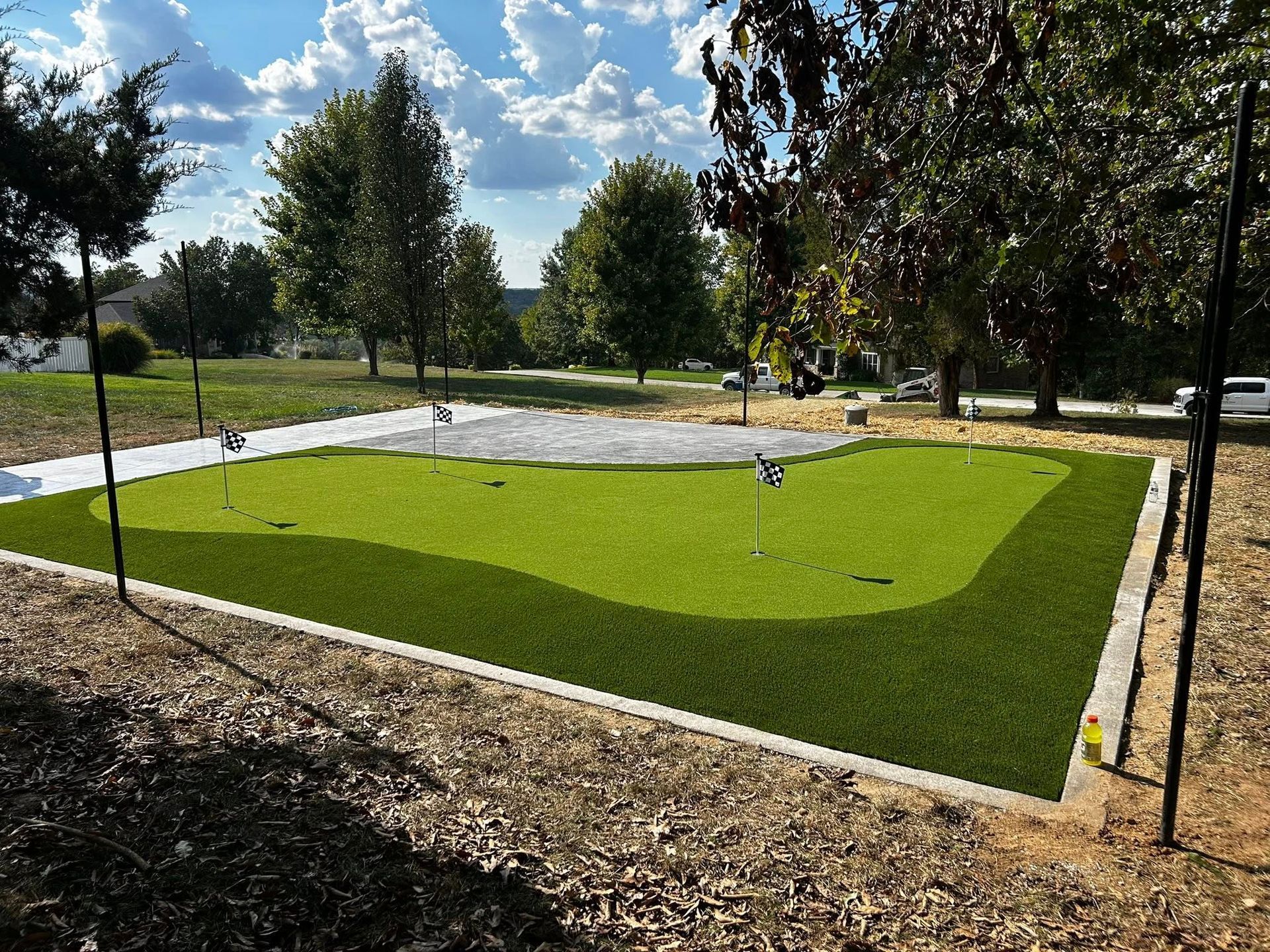 Small green artificial turf area bordered by mulch in a sunny park with trees and sky
