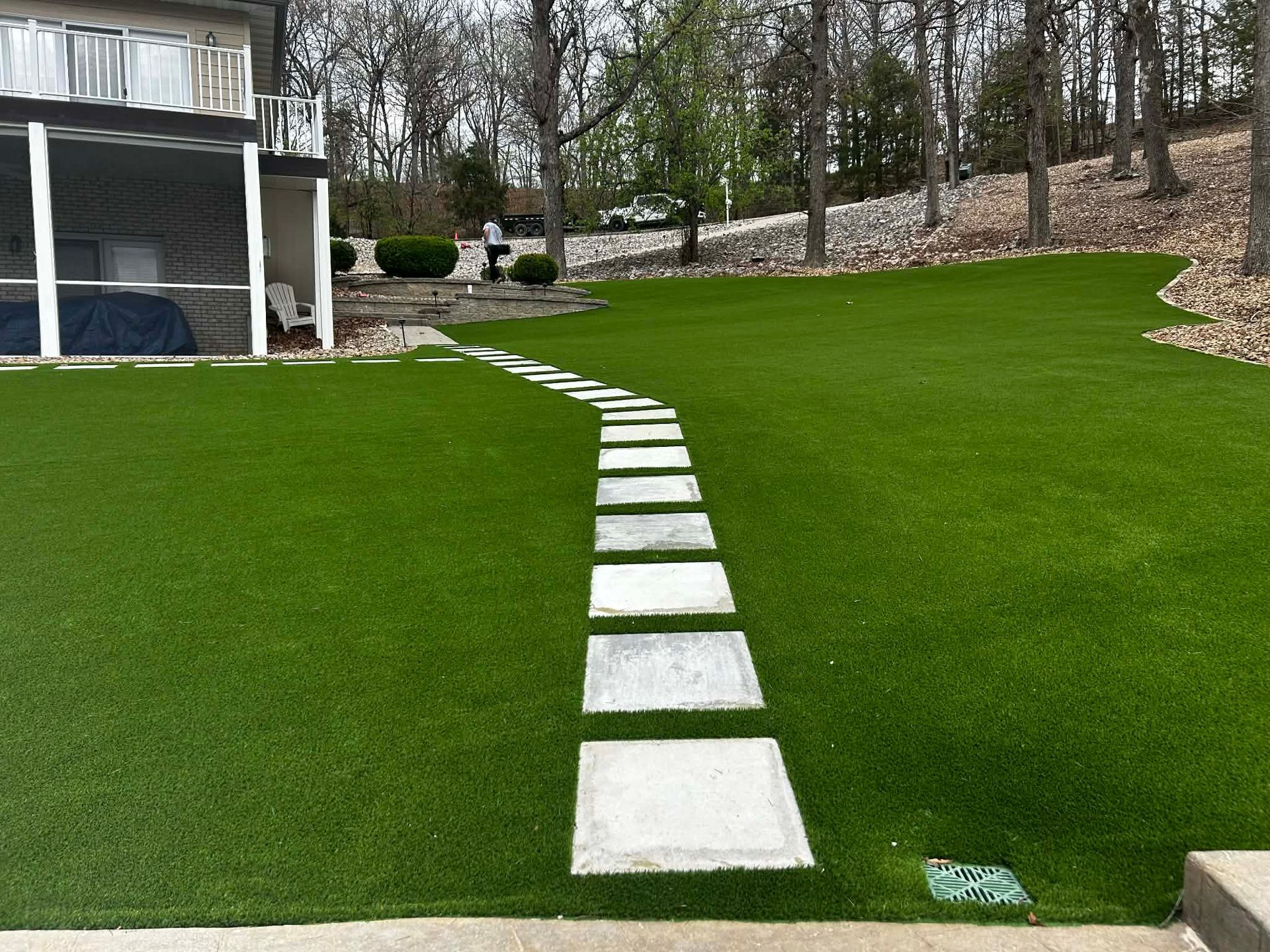 Backyard with white stepping stones winding up a steep green lawn beside a house and trees