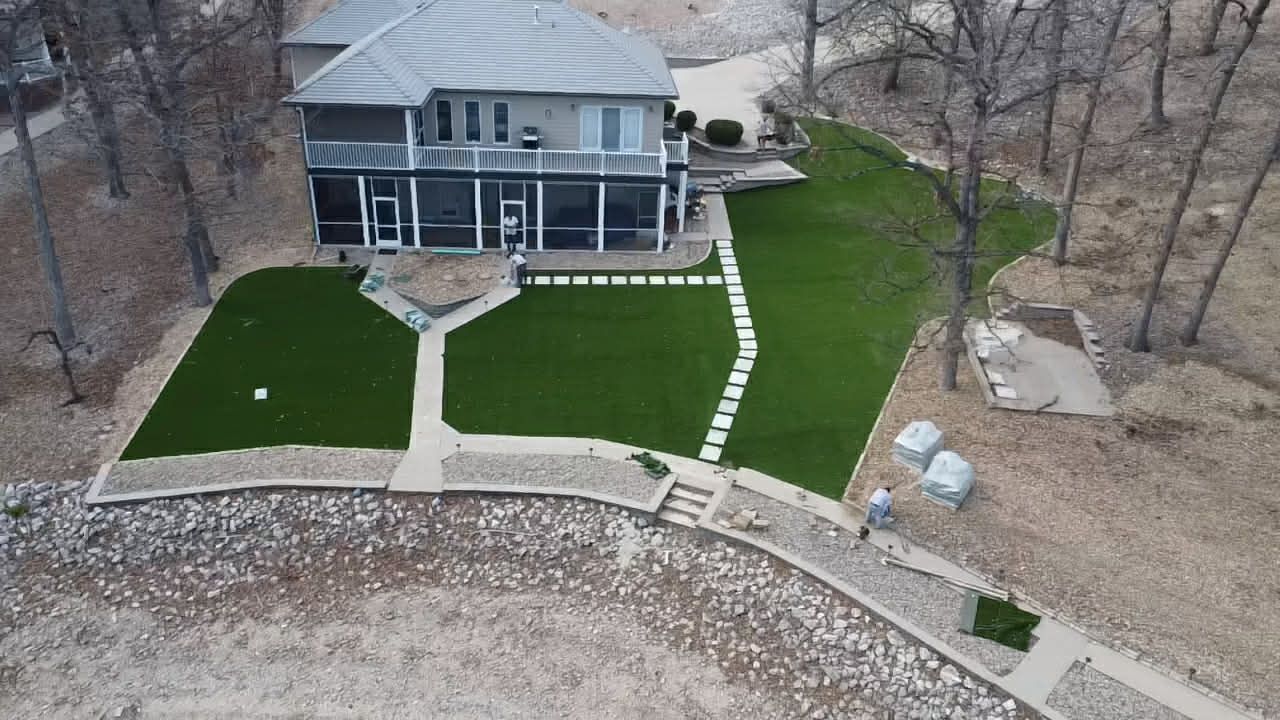 Aerial view of a house with a green landscaped yard, stone steps, and a curved retaining wall.