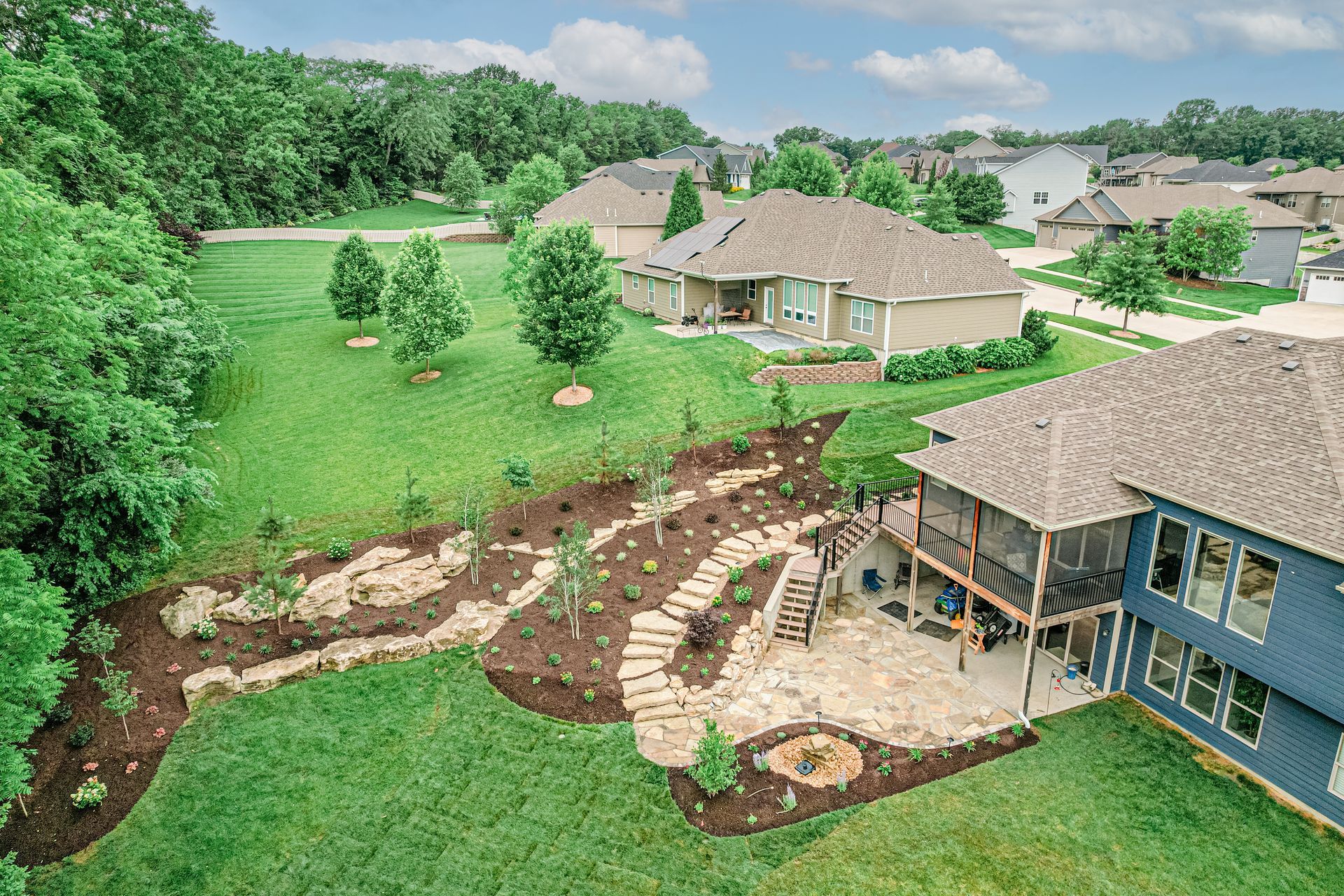 Backyard with winding stone path, gazebo, lush green lawn, and neighboring homes under a clear sky