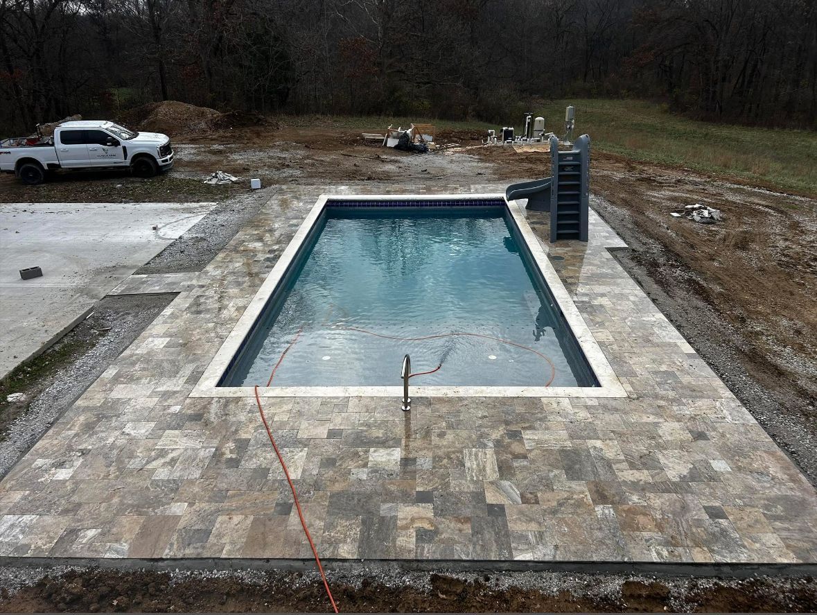 Rectangular swimming pool with stone pavers, outdoors in a yard under construction, with a pickup truck nearby