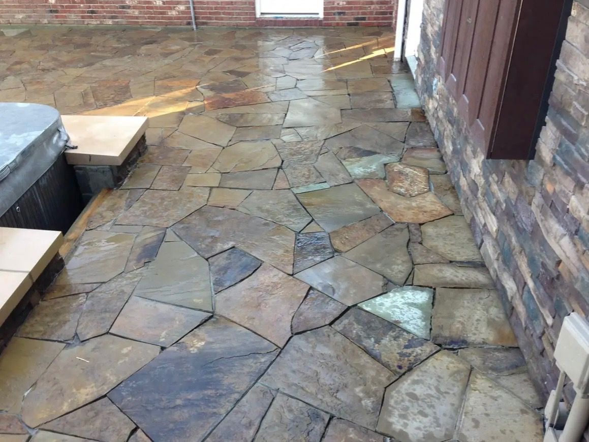 Stone patio walkway beside a brick wall, with scattered flagstones and wet patches