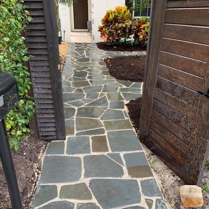 Stone walkway leading to a front door, bordered by dark wood fencing and garden plants