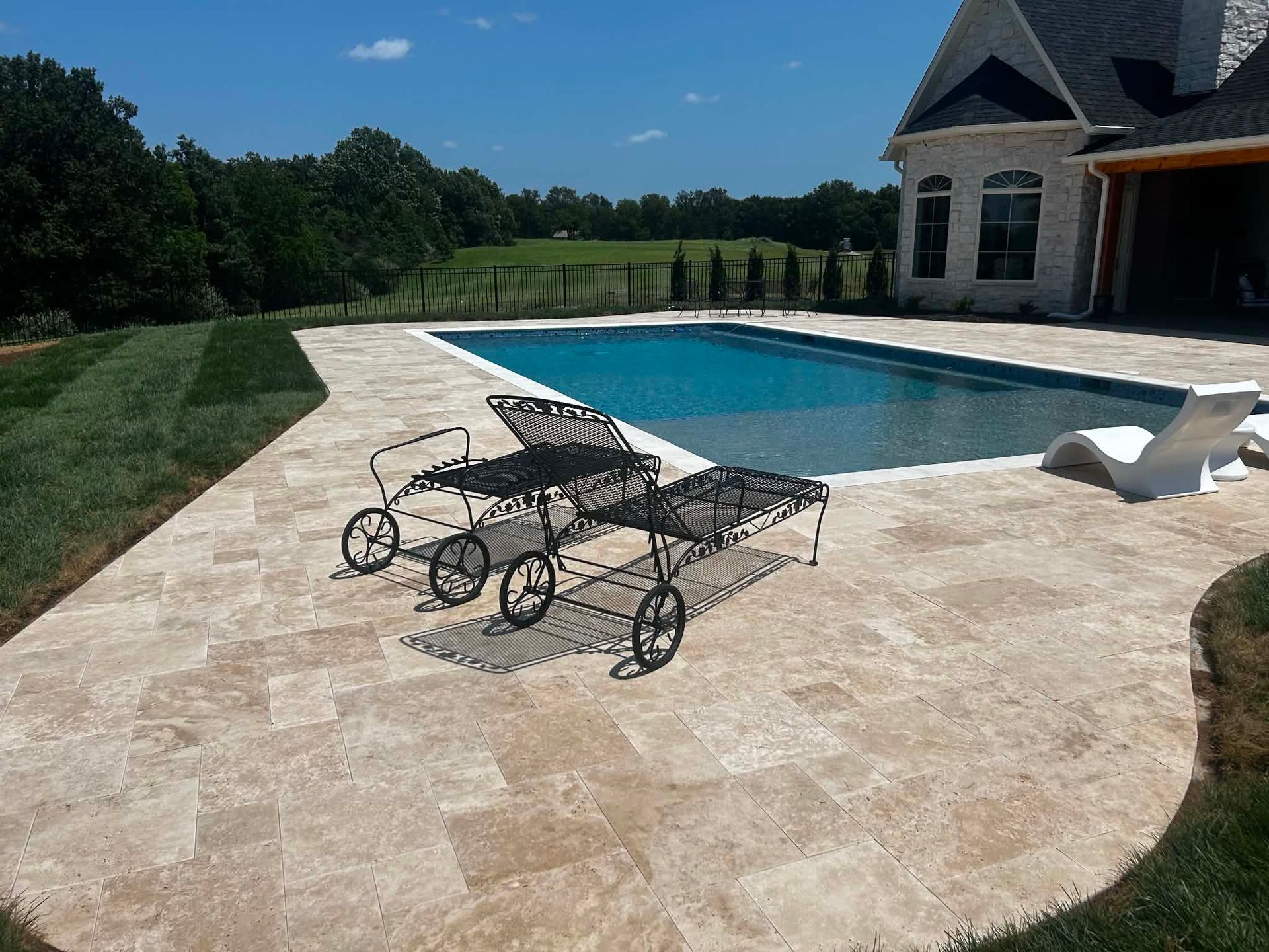 Backyard pool with stone patio, lounge chairs, and a small pavilion under a blue sky
