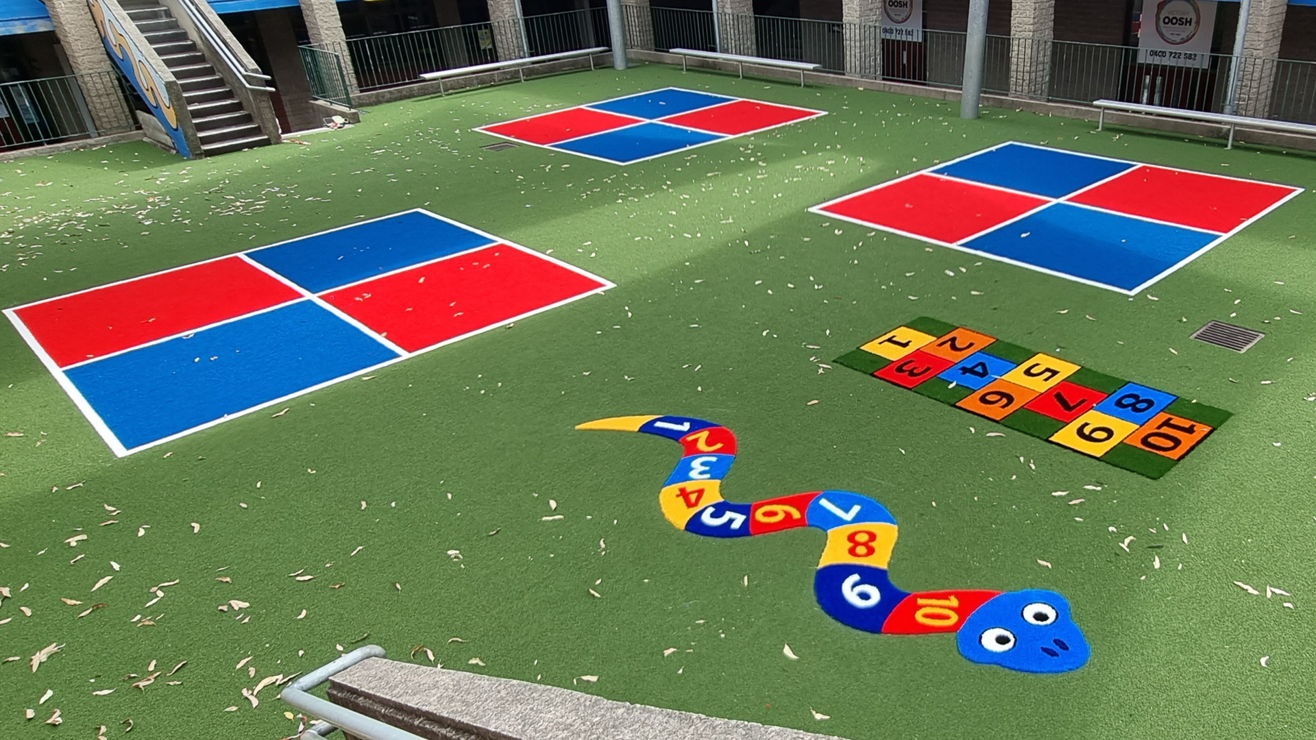 Outdoor play area with colorful numbered mats and stepping stones on grass, including red and blue square panels.