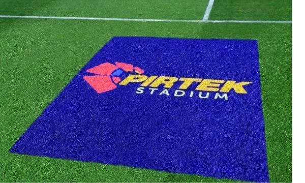 Purple stadium logo on green turf reading “Patek Stadium” near a white field line