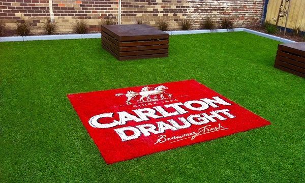 Red Carlton Draught logo on a green lawn beside a brick wall and wooden bench