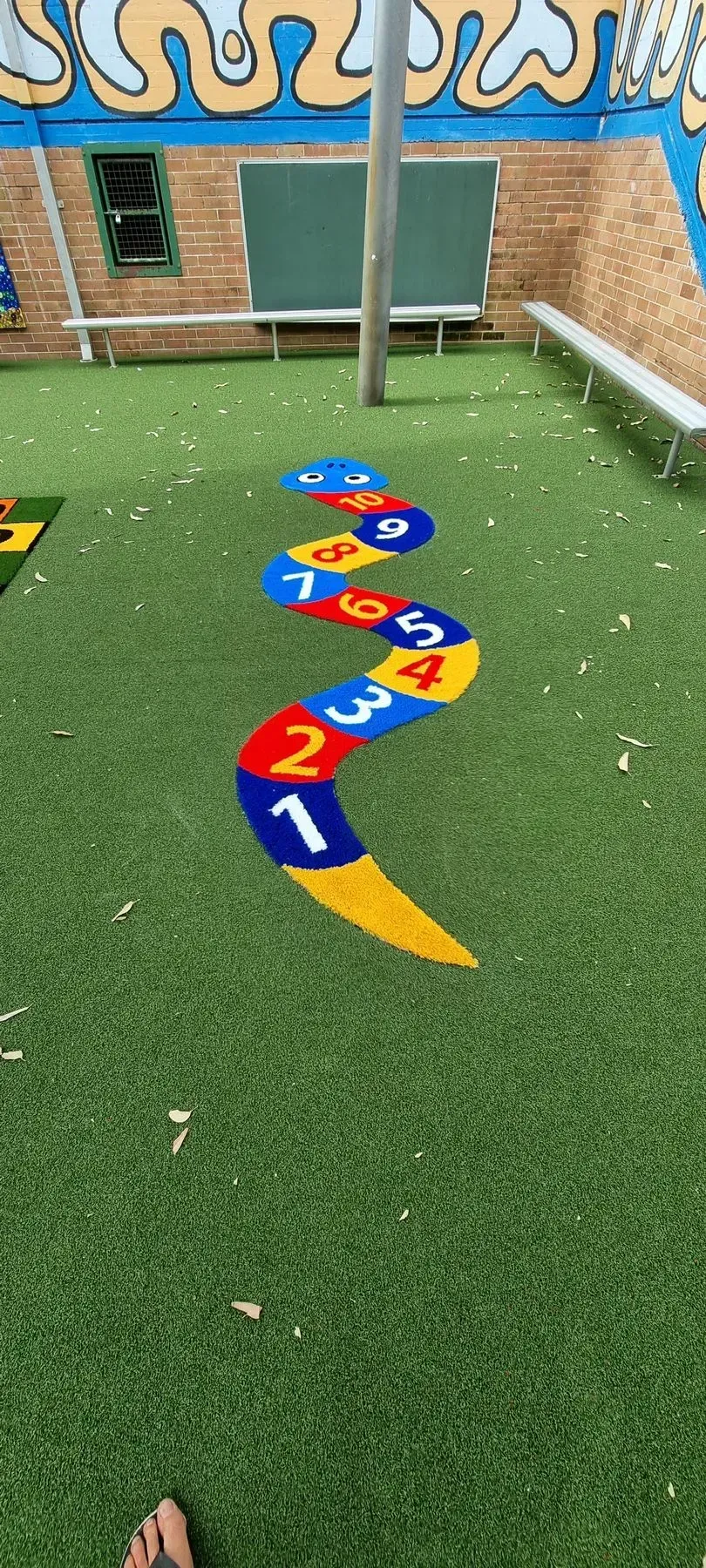 Colorful hopscotch-style number path on artificial turf in an outdoor playground area.