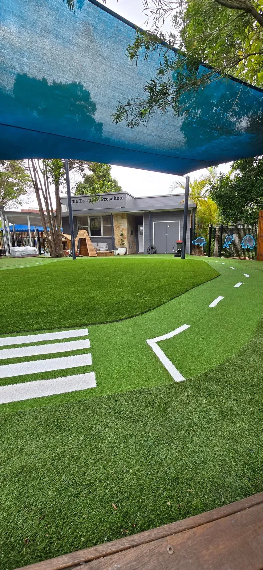 Outdoor mini golf course with green turf, white markings, and shaded trees near a building