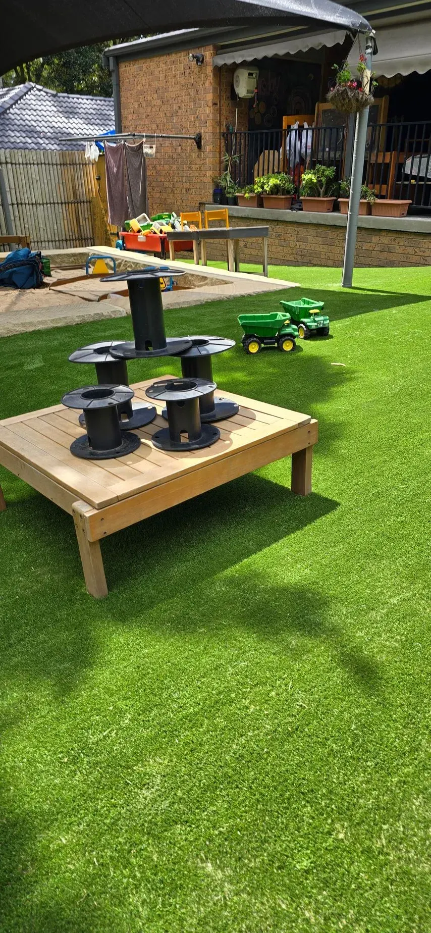 Wooden play table with black stepping blocks on bright green artificial grass in a backyard garden
