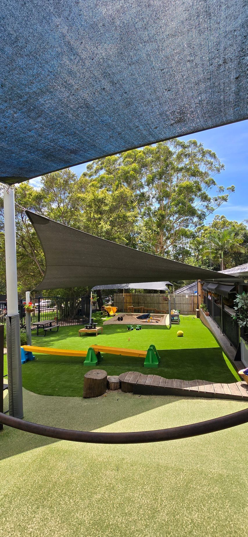 Outdoor mini-golf course with green turf, sand traps, and shade sails under trees