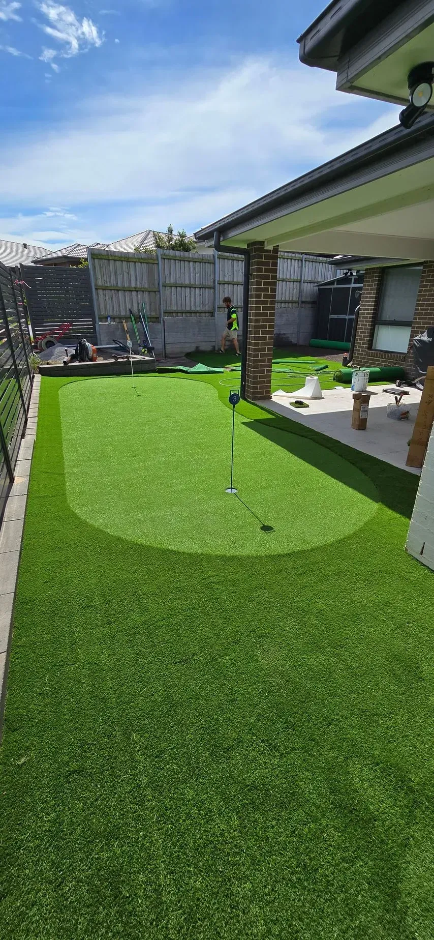 Backyard with bright green artificial grass, covered patio, and a small paved seating area