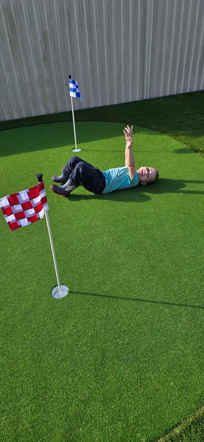 Person lying on green grass near small red-and-white flags and a blue-and-white pole on a lawn.