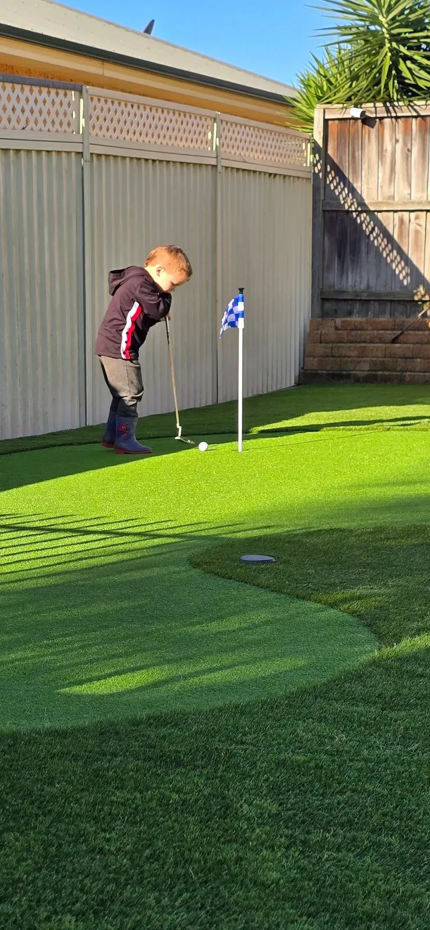 Person lining up a putt on a backyard putting green beside a flag and cup at sunset