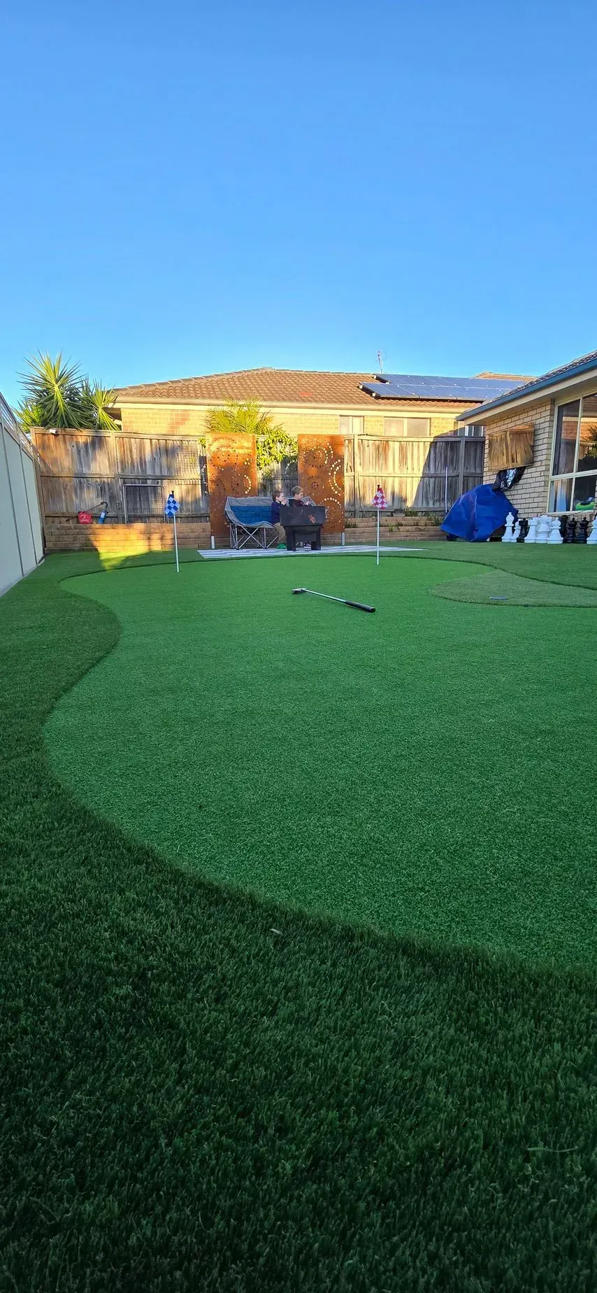 Backyard with green turf lawn, blue sky, and a house patio in warm sunlight