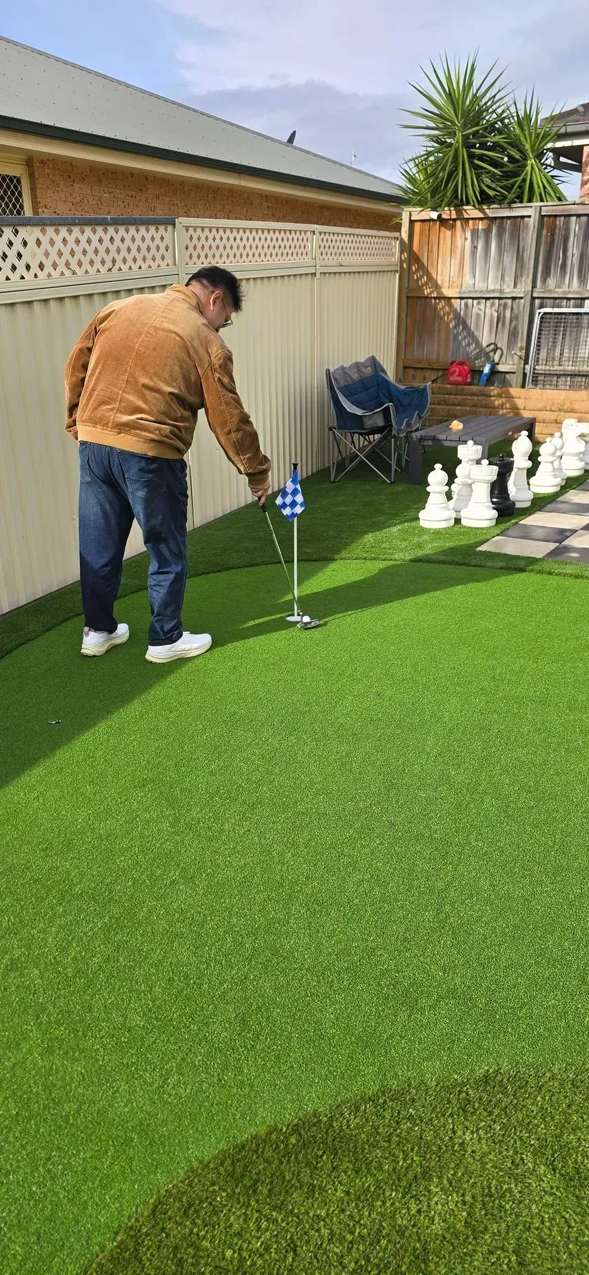 Person putting on golf green in a backyard with a practice hole and golf balls nearby